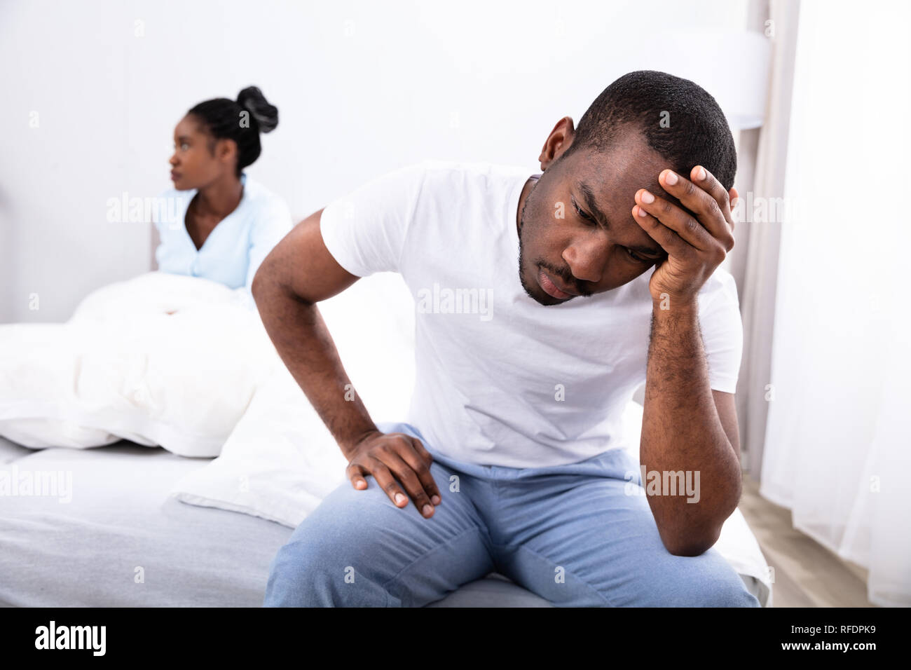 Verärgert jungen afrikanischen Mann sitzt auf dem Bett vor den Augen seiner Frau Stockfoto