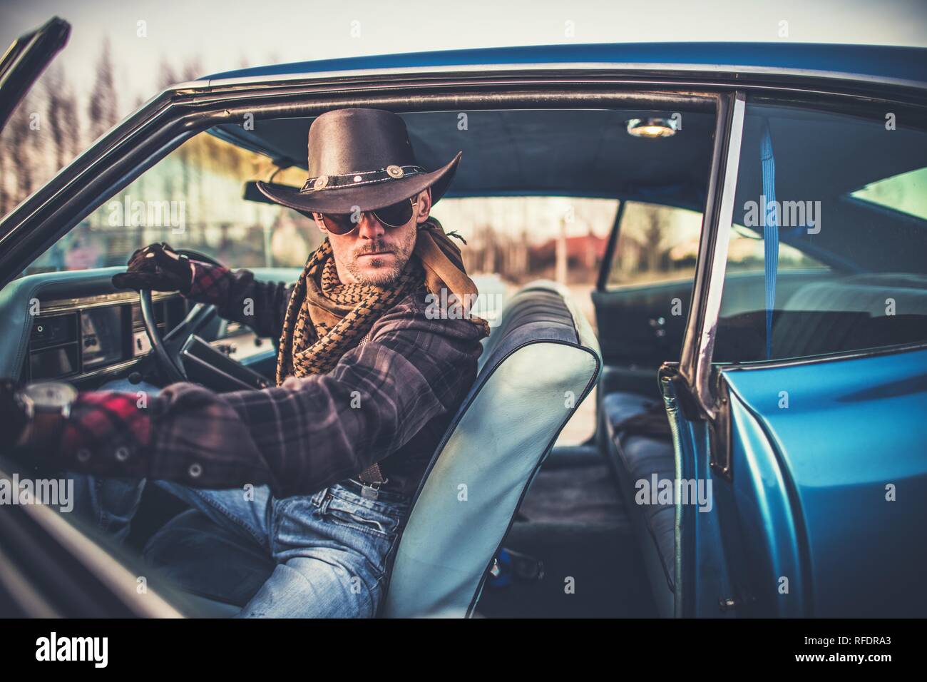 Cowboy im Auto. Kaukasische Männer tragen im westlichen Stil hat in seinem klassischen Fahrzeug. American West Konzept. Stockfoto