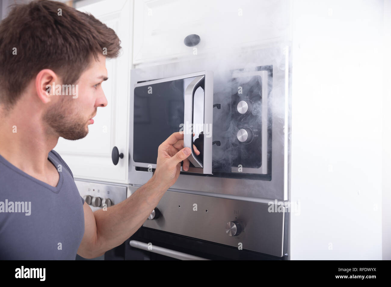 Erstaunt Mann, der vor dem Holzofen mit Rauch um Küche Stockfoto