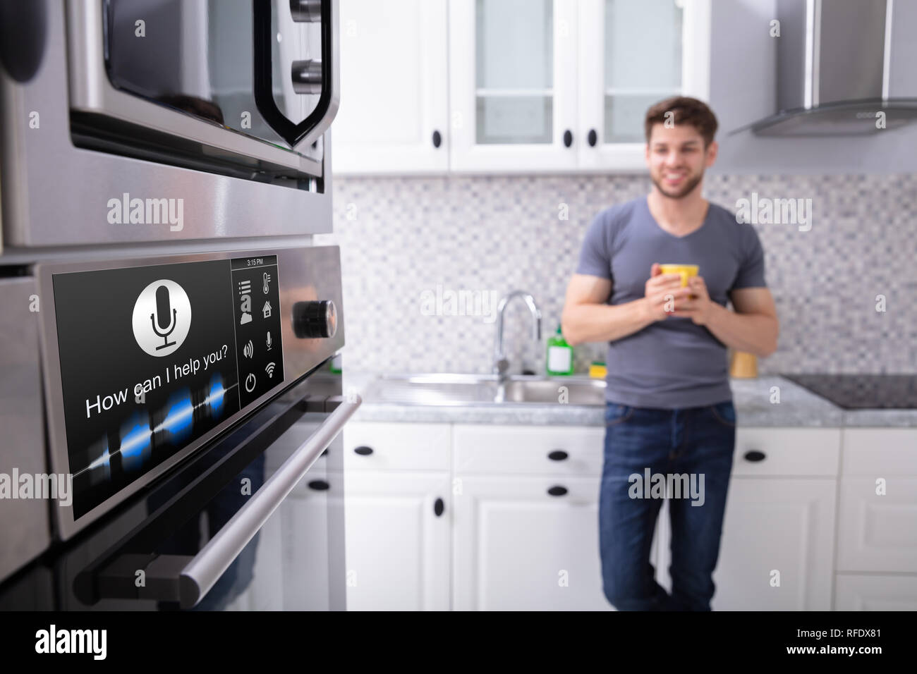 Glücklich, junger Mann auf der Suche nach Ofen mit Spracherkennung in der Küche Stockfoto
