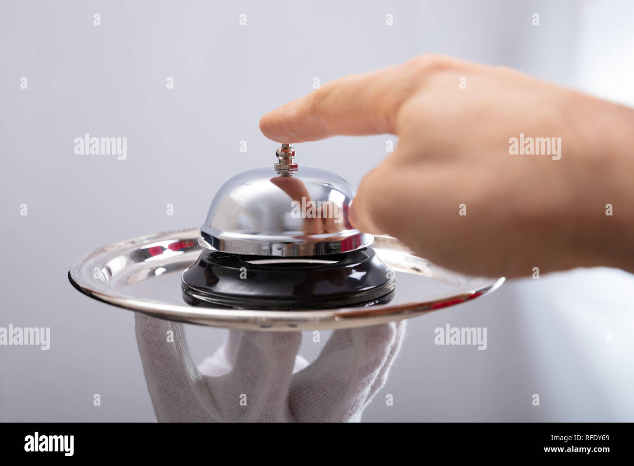 In der Nähe der Person Hand Ringing Service Bell auf der Platte, die Kellner Stockfoto