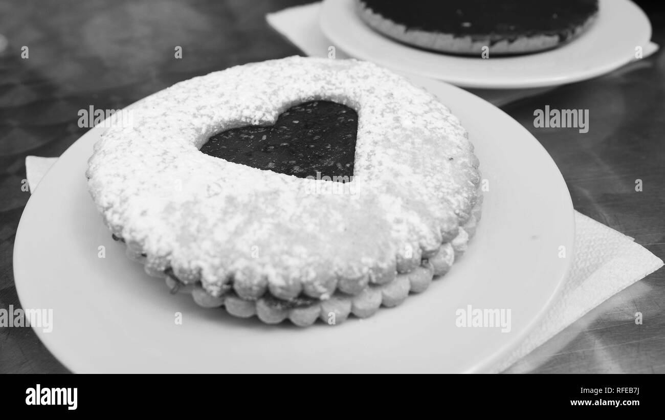 Ein Schwarzweiß-Foto von einem Cookie mit einem Herzen Dekoration mit Marmelade gemacht und mit Puderzucker bestreut auf einer Platte. Stockfoto