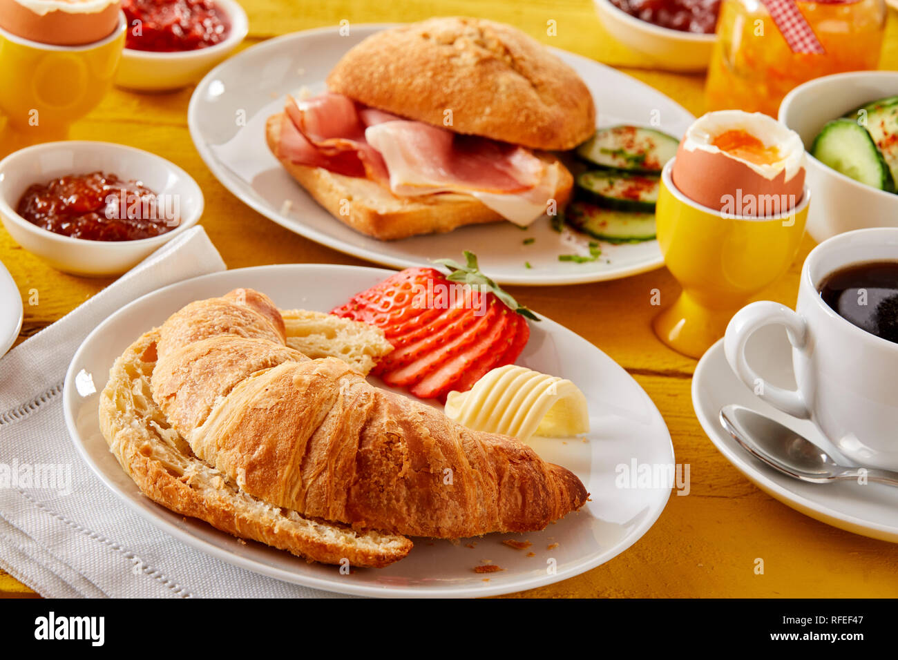 Frisch gebackene Croissant mit Butter und Erdbeere serviert mit Speck, gekochte Eier, Kaffee und Gelees oder Konfitüren für eine köstliche Frühling Frühstück Stockfoto