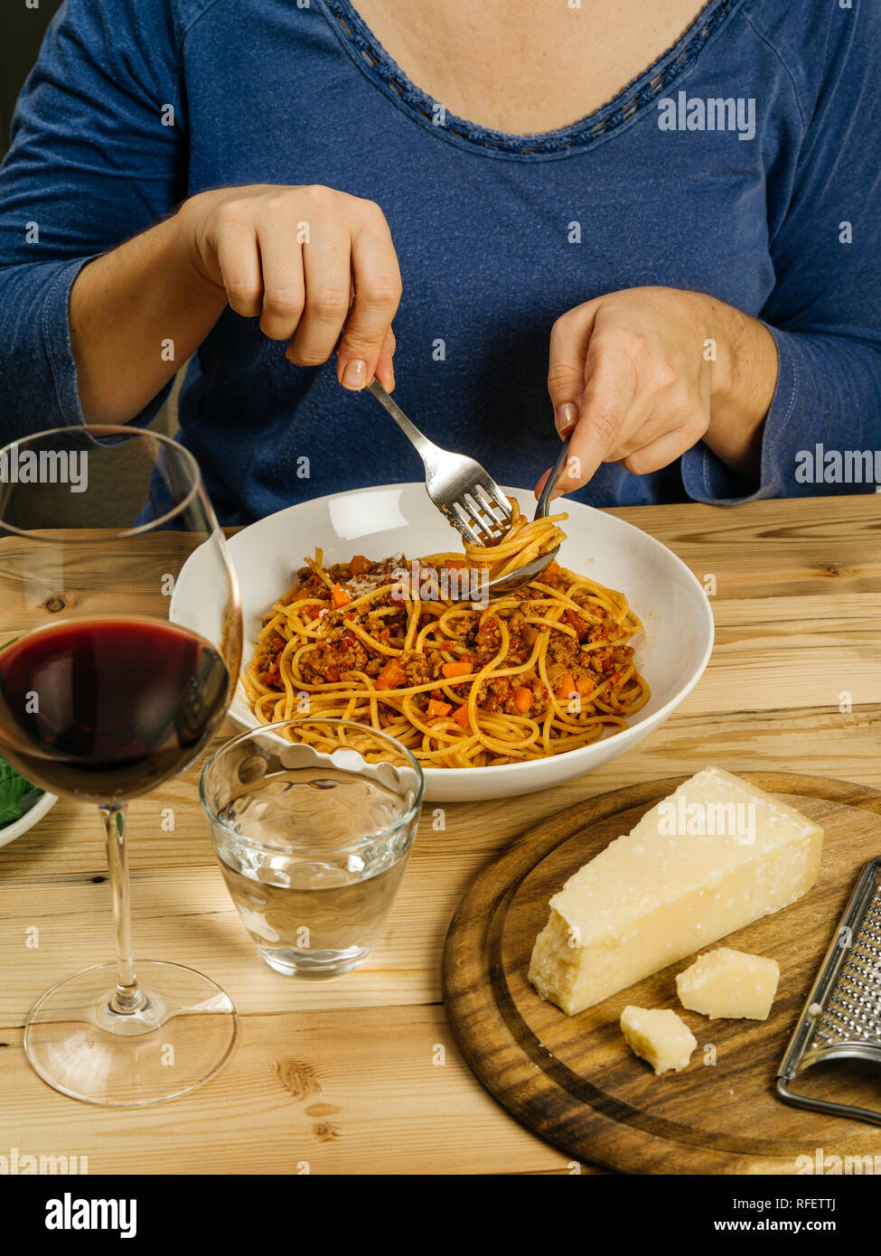 Foto einer Frau essen eine Schüssel mit traditionellen Spaghetti Bolognese mit einem Glas Rotwein über rustikale Tabelle. Stockfoto