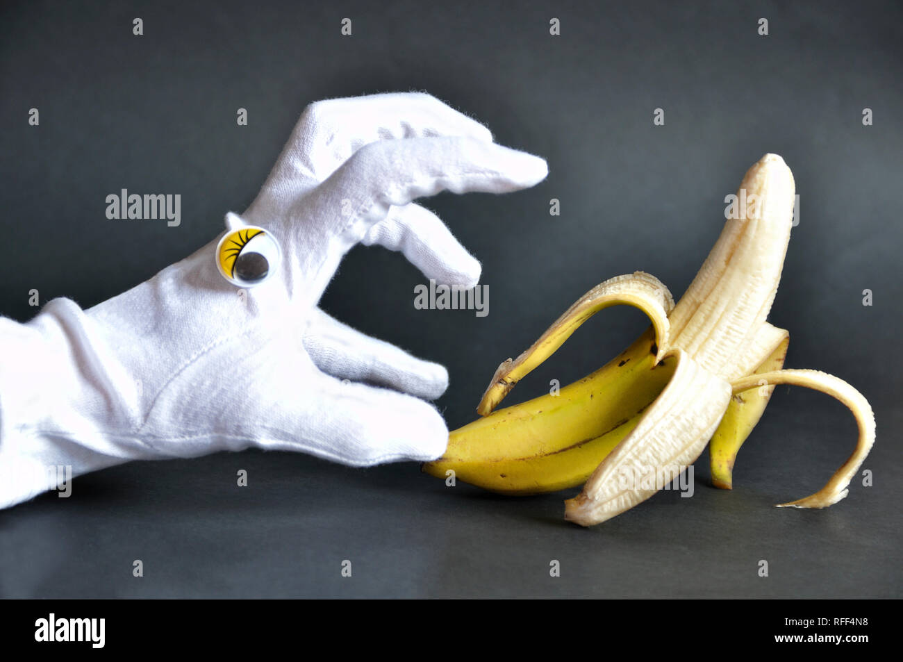 Lustige Foto von einer Hand Tragen eines weißen Handschuh mit Augen, die versuchen, eine Banane zu fangen Stockfoto