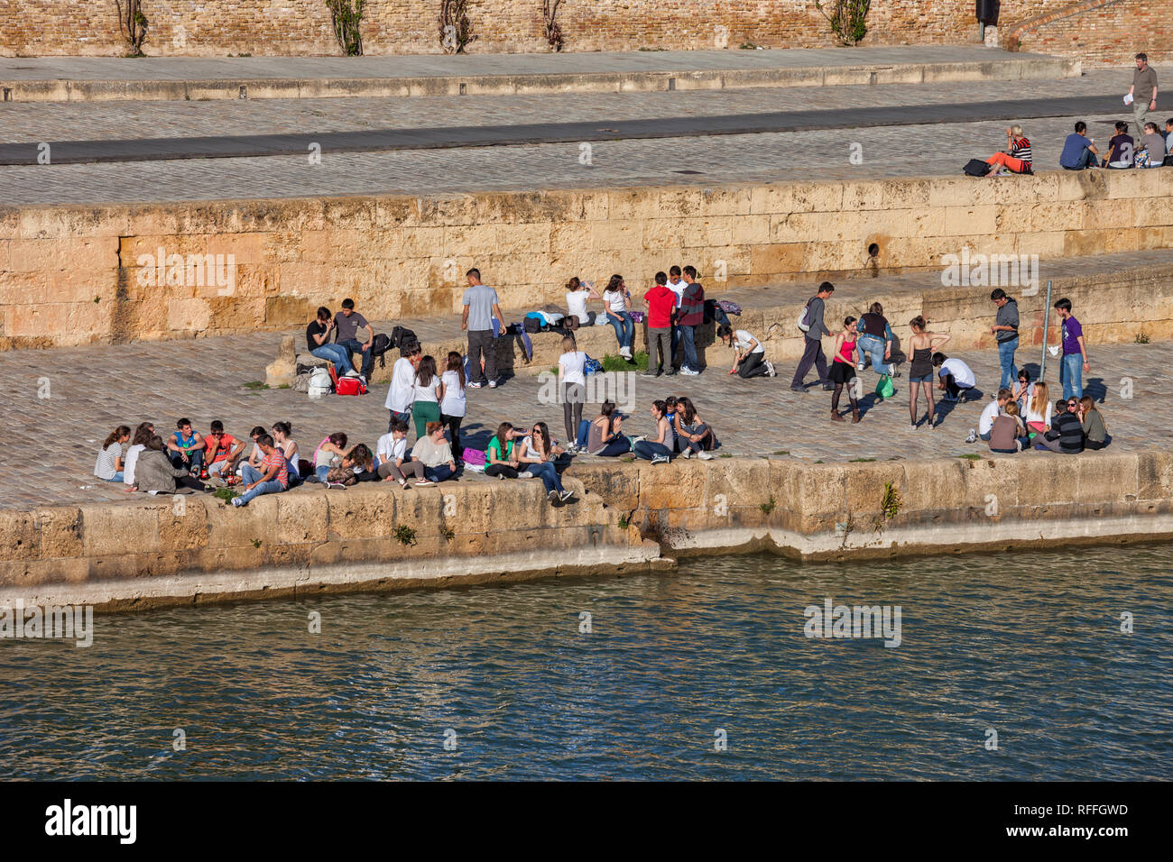 Gruppe von jungen Leuten, Studenten, hängen am Ufer des Flusses in der Stadt Sevilla in Andalusien, Spanien Stockfoto