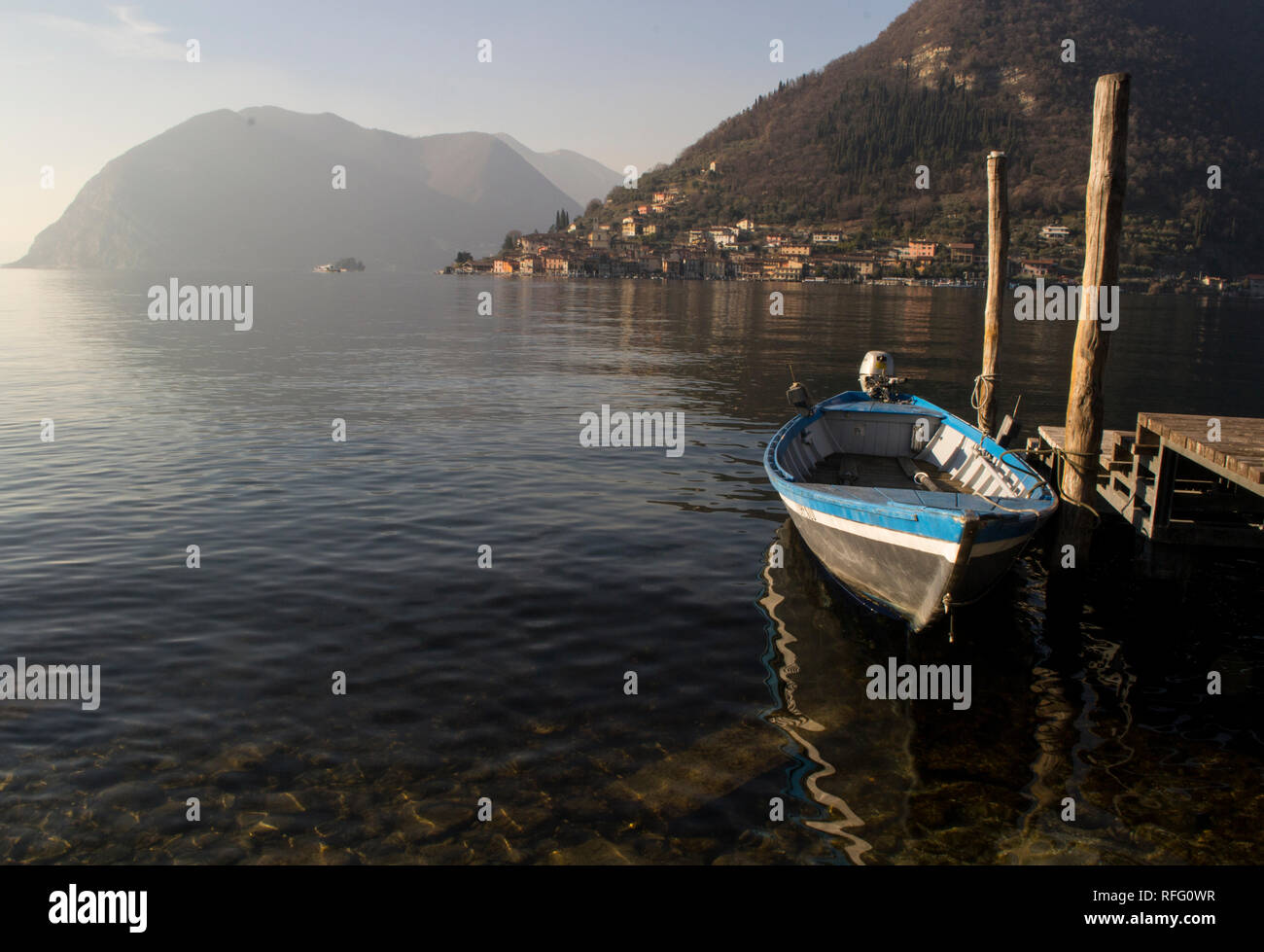 Kleines Boot in der Nähe von einem hölzernen Pier am Iseo See in Norditalien geparkt, mit Blick auf die Insel Monte Isola. Stockfoto