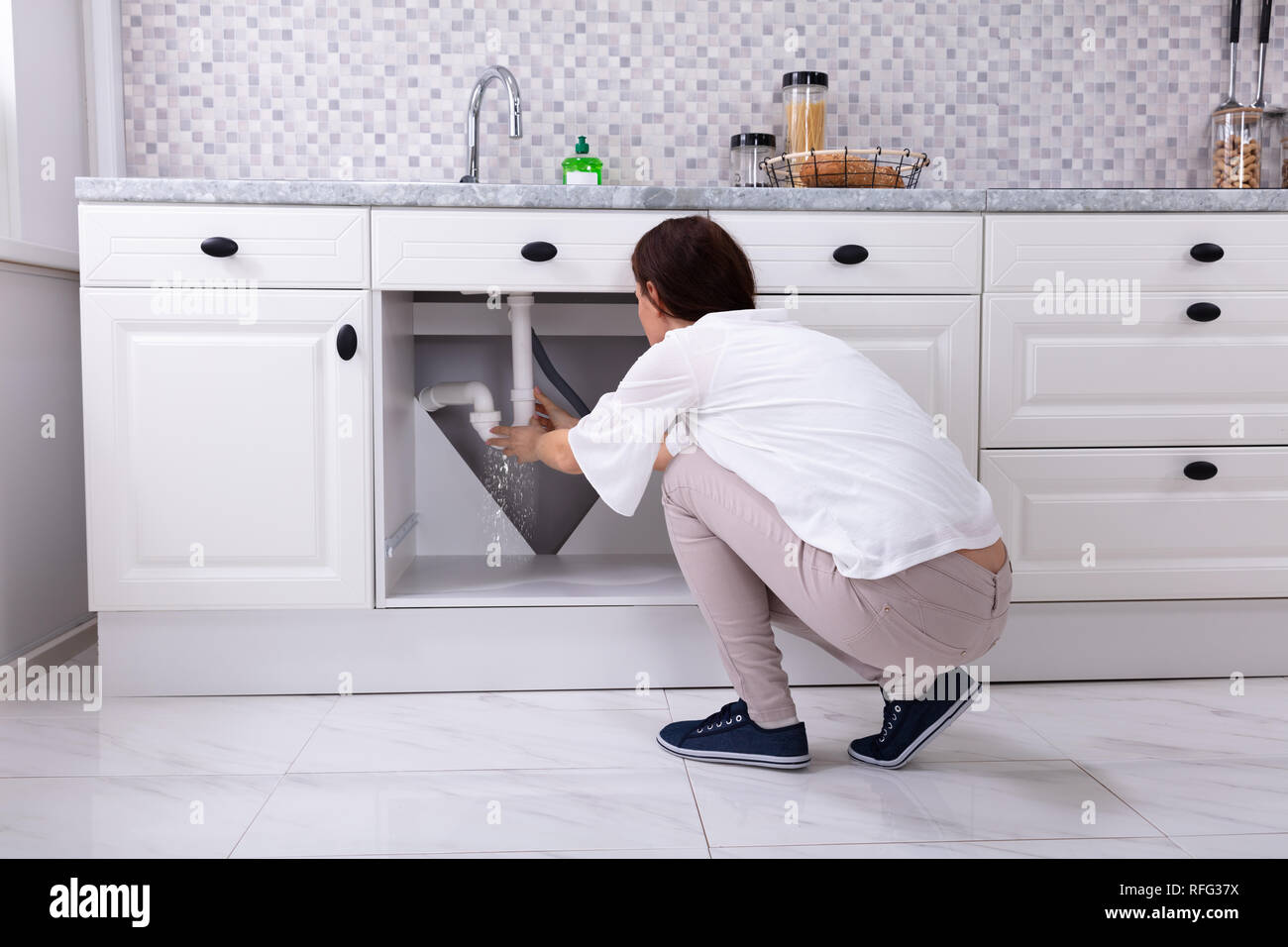 Rückansicht einer Frau Versuchen zu stoppen Wasseraustritt aus Waschbecken Rohr in der Küche Stockfoto