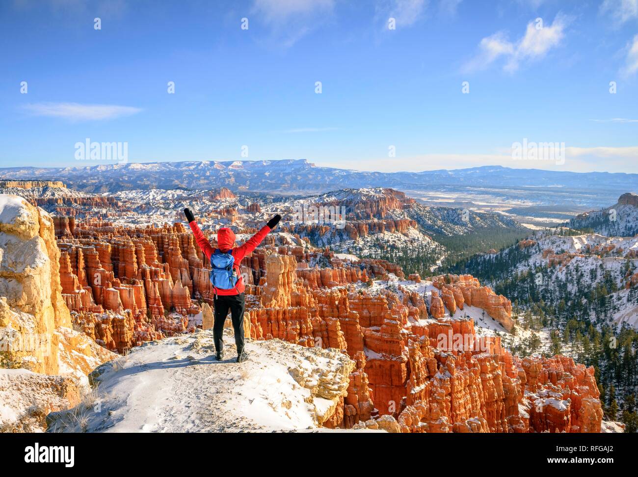 Junge Frau mit ausgestreckten Armen und Blick auf das Amphitheater, bizarr verschneite felsige Landschaft mit Hoodoos im Winter Stockfoto