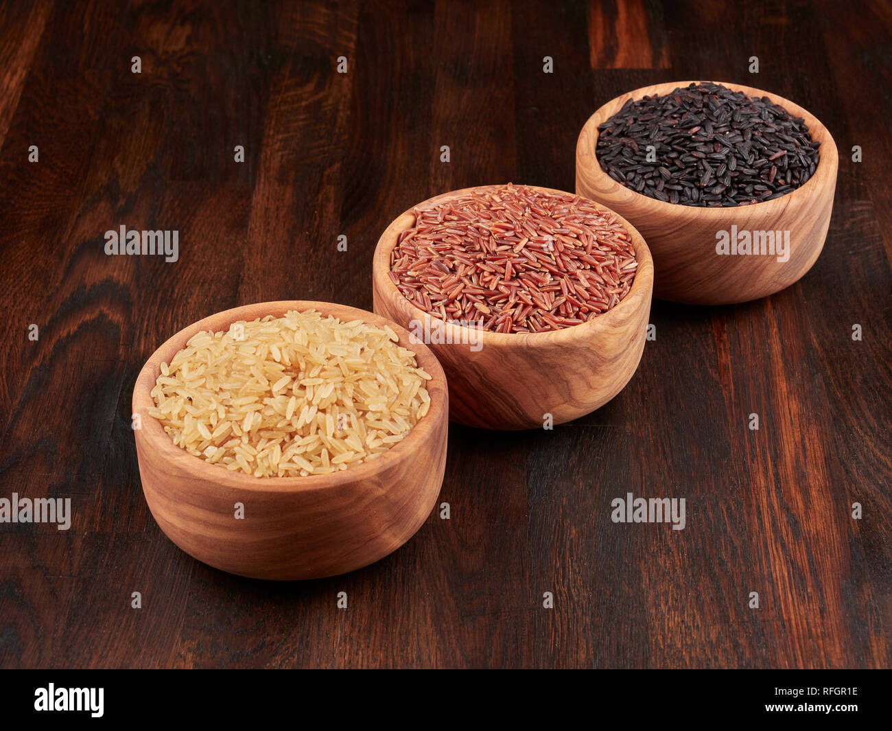 Ungekocht, schwarzen, roten und braunen Reis in Olivenöl Holz Schalen, auf einem dunklen Holzmöbeln im Landhausstil board Stockfoto