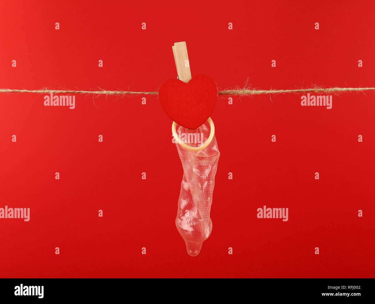 Schließen Sie ein Kondom hängen an Garn Wäscheleine mit Holz Wäscheklammer mit herzförmigen Schild über Roter Hintergrund mit Kopie Raum, Low Angle Seite vi. Stockfoto