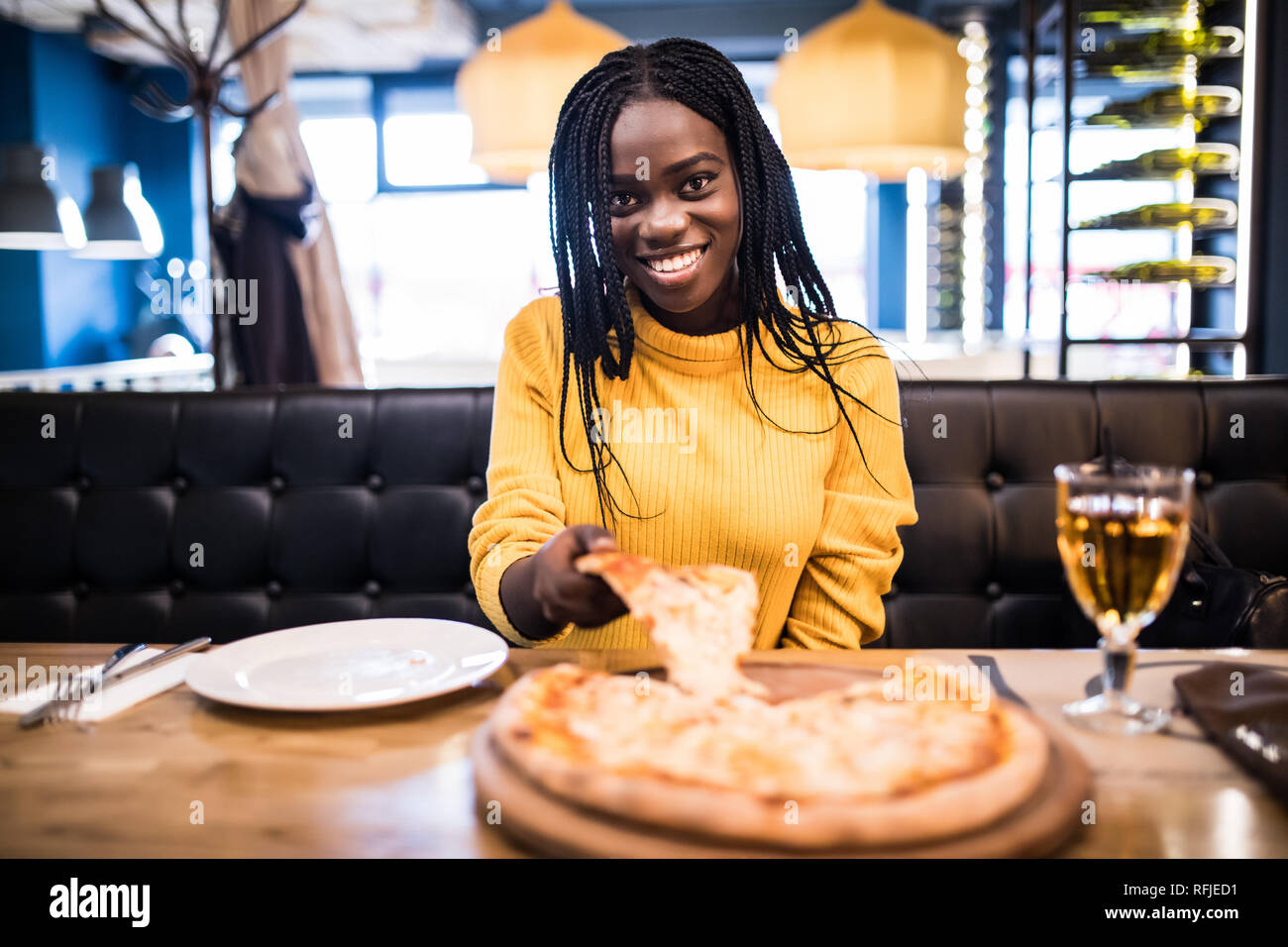 Junge afrikanische Mädchen in gelb Pullover essen Pizza im Restaurant. Stockfoto