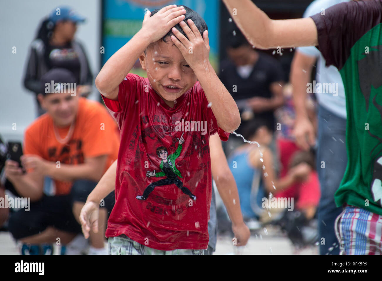 Einem getränkten nasse Junge in ein rotes Hemd spielen an einem Brunnen in heissen Sommertag. San Jose, Costa Rica Stockfoto