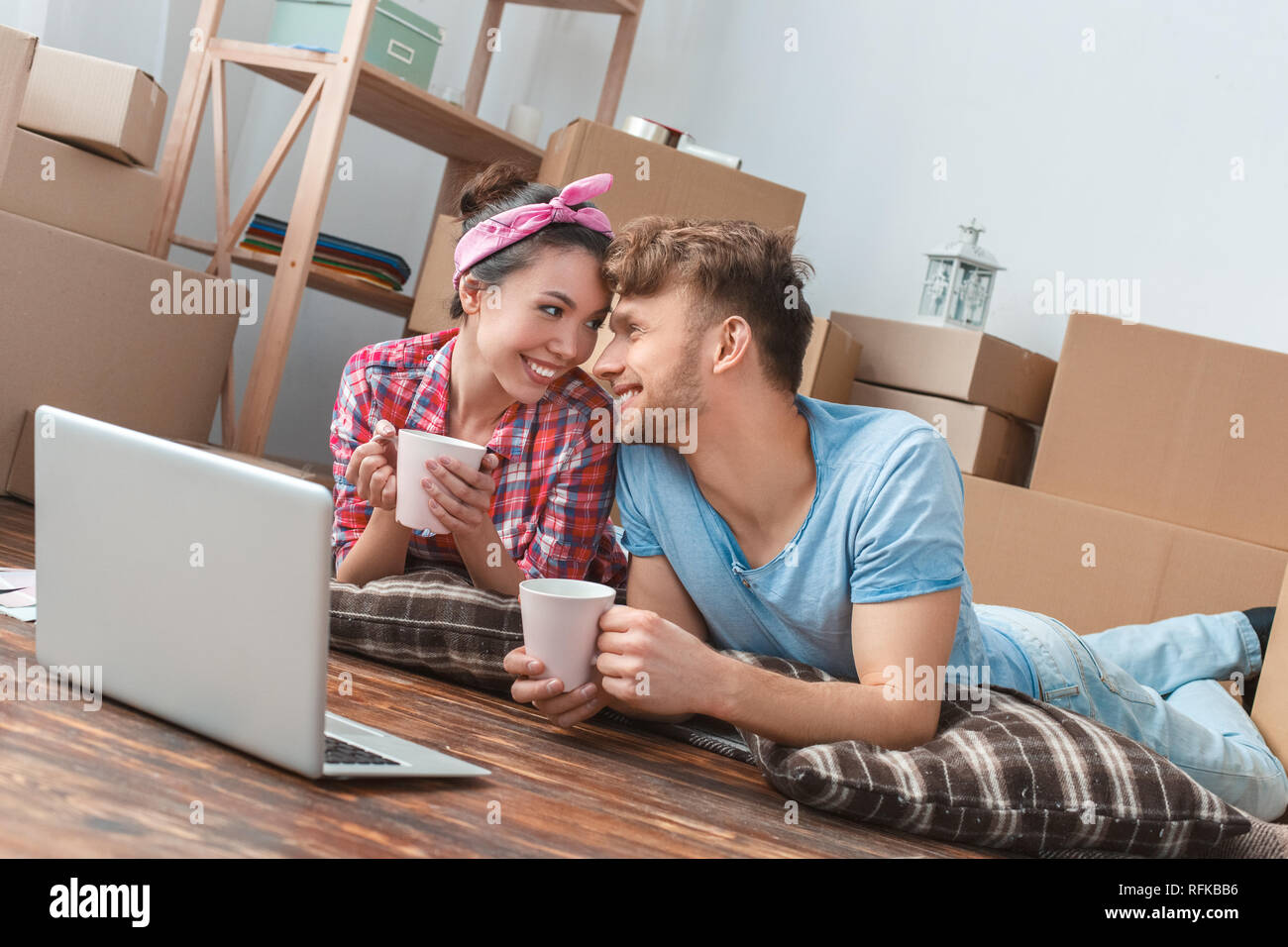 Junges Paar nach New liegend mit Laptop holding Tassen für Tee an jedem anderen spielerischen Nähe suchen Stockfoto