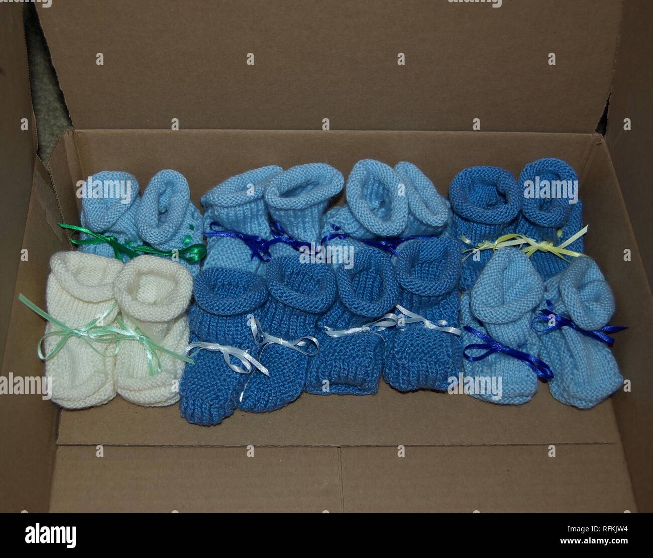 Gestrickte Junge Baby Booties mit Bändern aufgereiht in einer Reihe - Farben: Hellblau, Dunkelblau, Weiß Stockfoto