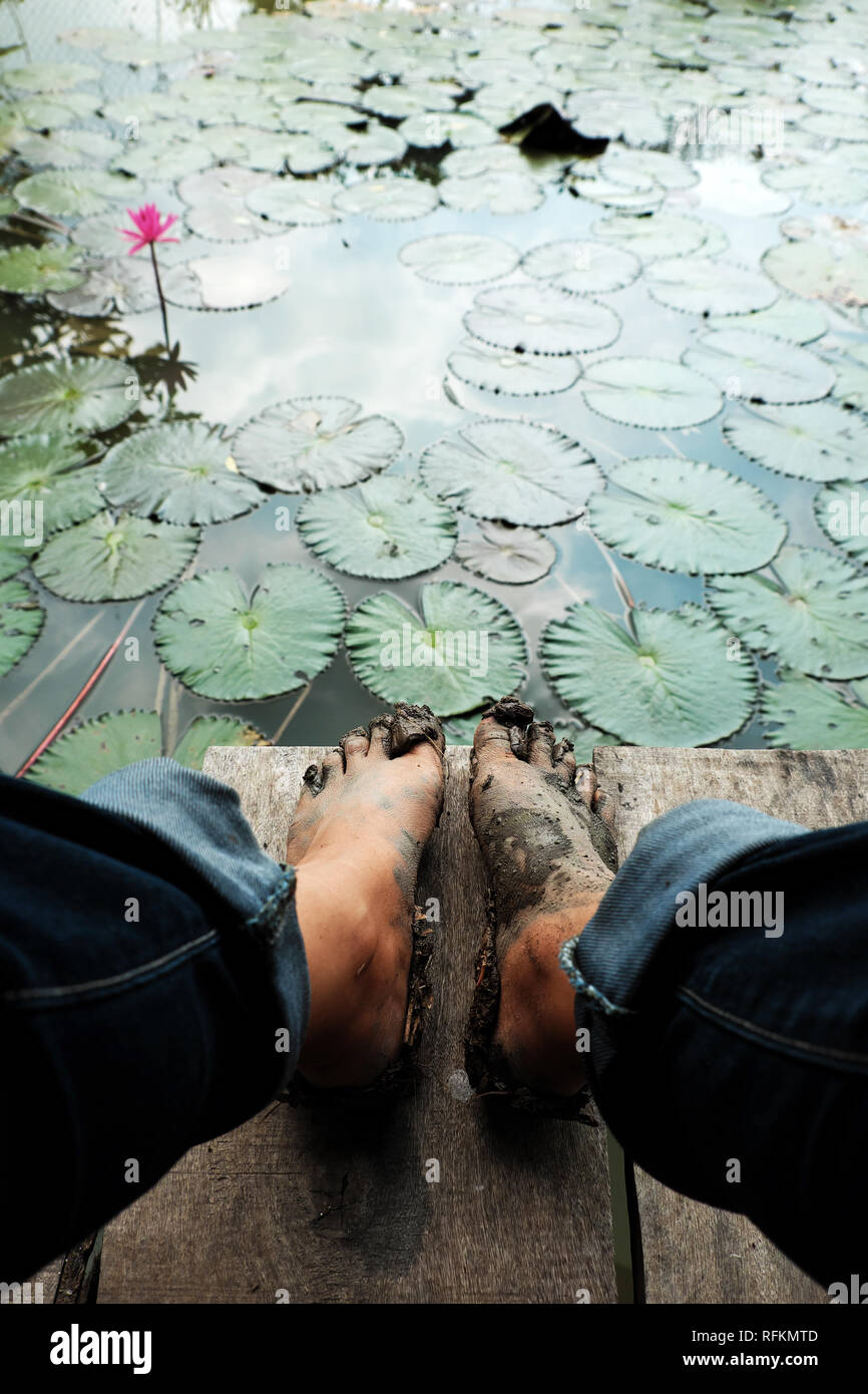 Genießen Sie im Sommer an der Vietnamesischen Landschaft des Mekong Delta, Frauen tragen Jeans mit den Füßen im Schlamm, sitzen auf hölzernen Stock in der Nähe von Seerosenteich, Oberfläche o Stockfoto