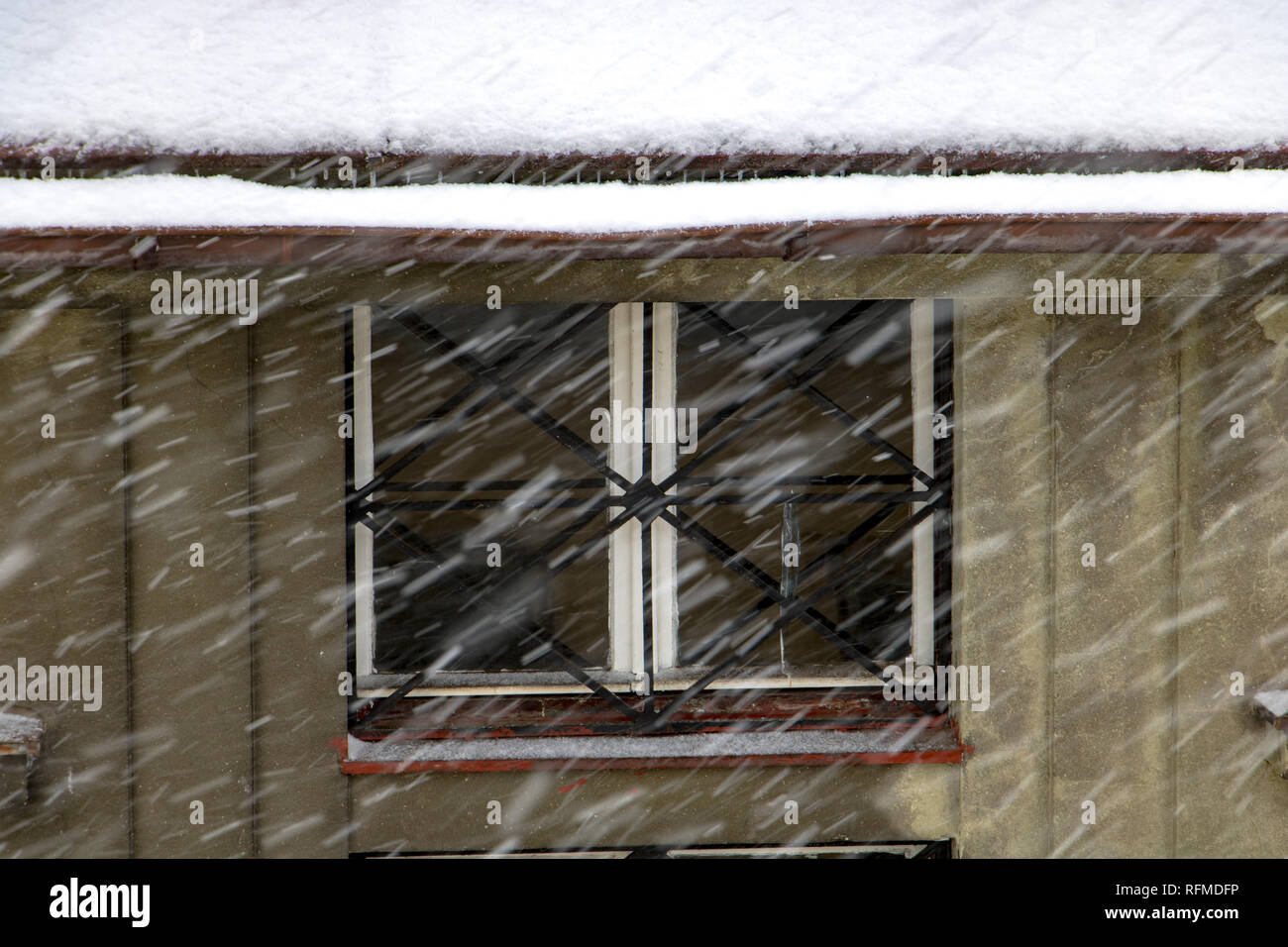 Der Schnee fällt vor den Fenstern des Hauses. Schneeflocken fliegen in der Stadt die Straße. Schneesturm in der Stadt. Stockfoto