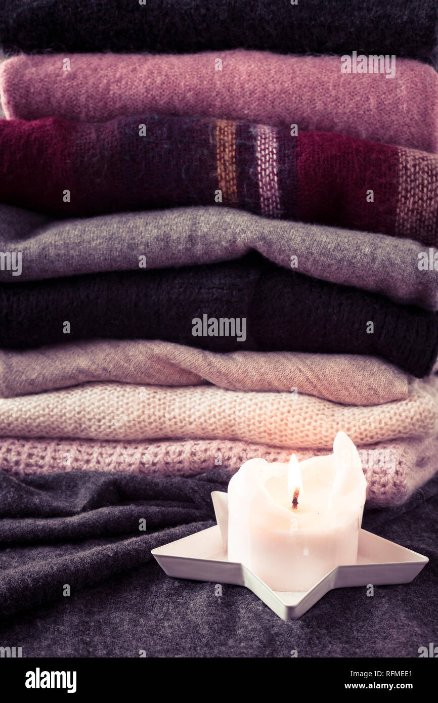 Stapel von rosa und grauen pullover mit leuchtenden Kerze, gemütlichen Winter Hintergrund oder Tapeten. Vertikaler, rosa Filter. Stockfoto