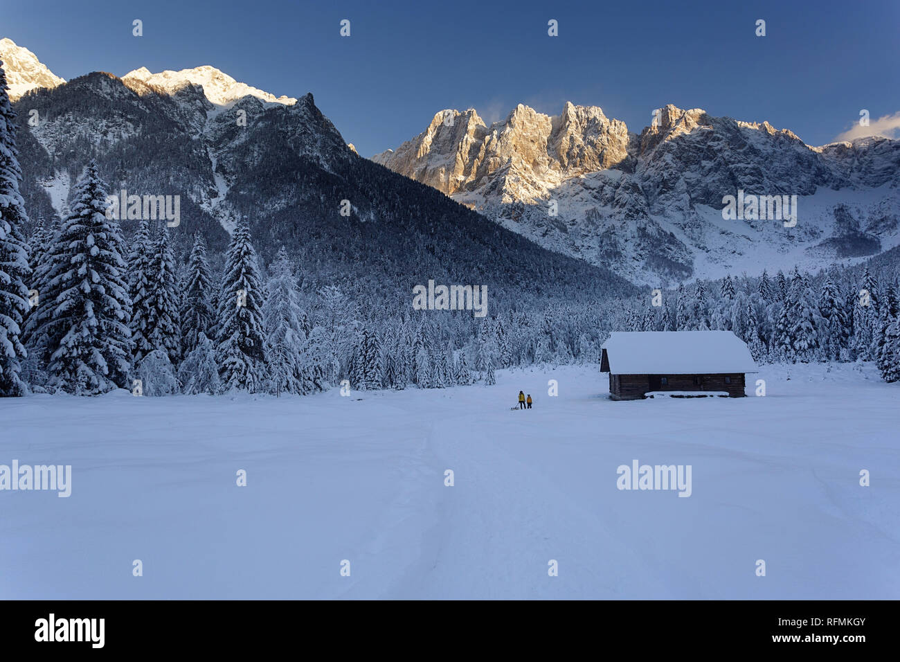 Mutter und Sohn wandern im Winter märchenhafte Landschaft mit Schlitten, Holzhütte und die Berge im Hintergrund, Slowenien, Krnica Stockfoto