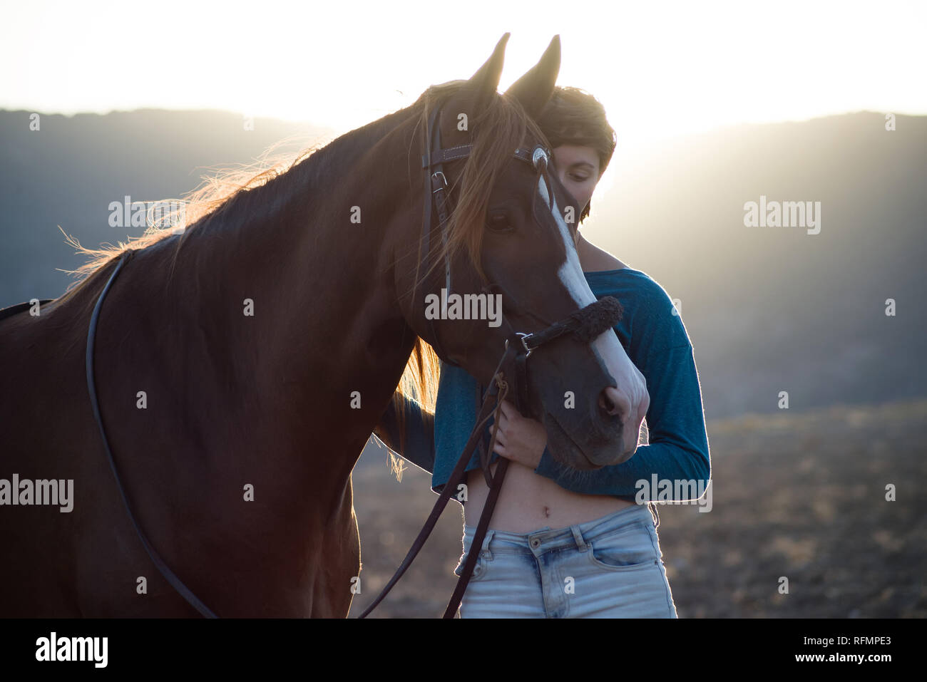 Teenage girl Streicheln, ein Pferd in den Sonnenuntergang mit einem unscharfen Hintergrund der Feld- und Berge Stockfoto