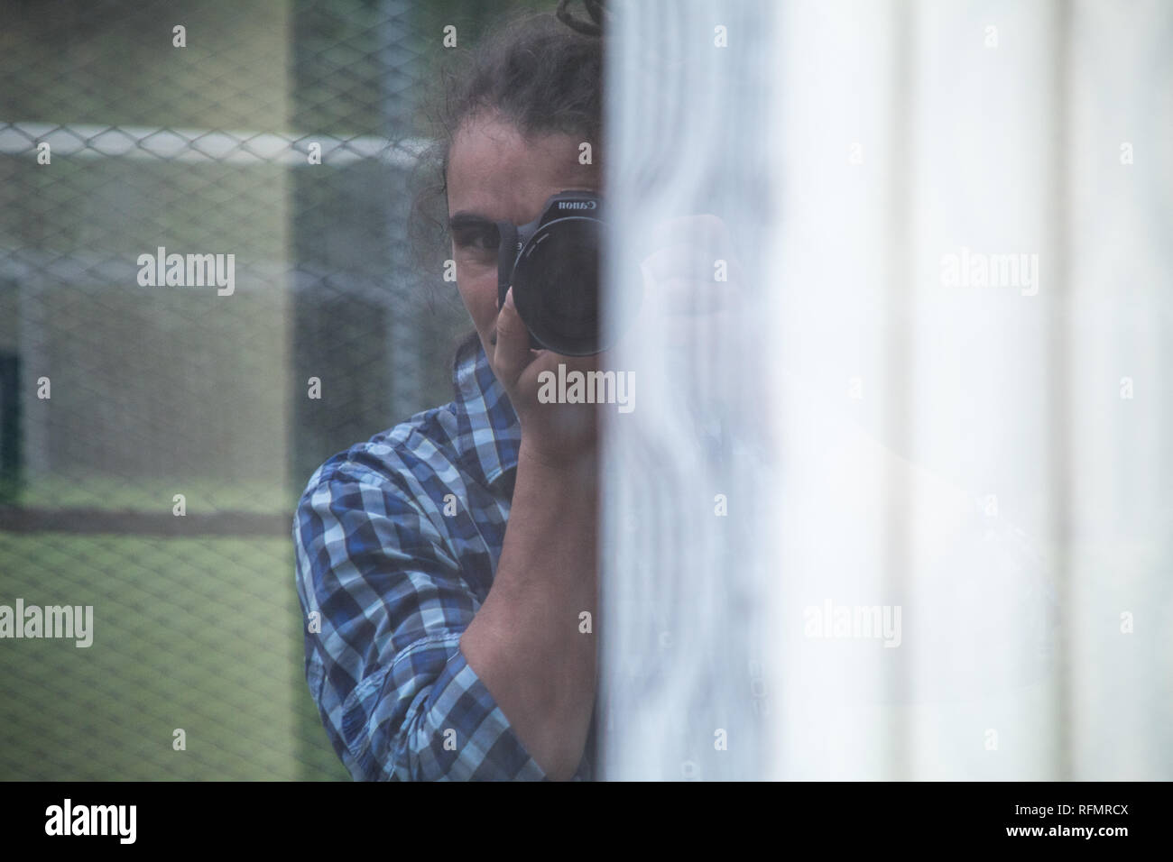 Ein Selbstportrait (Reflexion auf ein Fenster) eines männlichen Fotografen mit Dreadlocks eine alte Canon EOS 500D Kamera Stockfoto