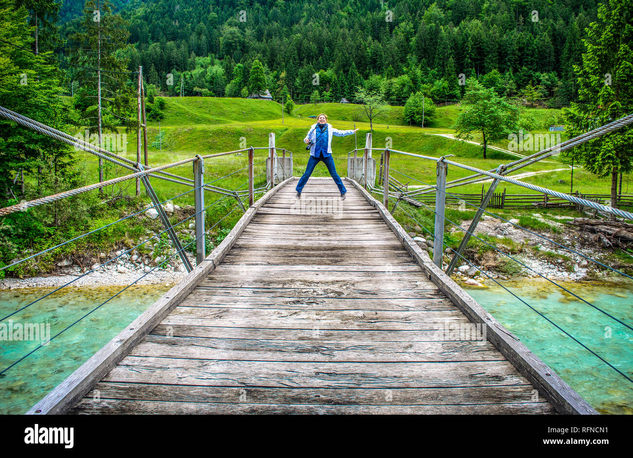 Gerne ferne Frau springen von einer hölzernen Fußgängerbrücke Fußgängerbrücke über den Fluss Soca in Slowenien in der wilden Natur Hintergrund Stockfoto