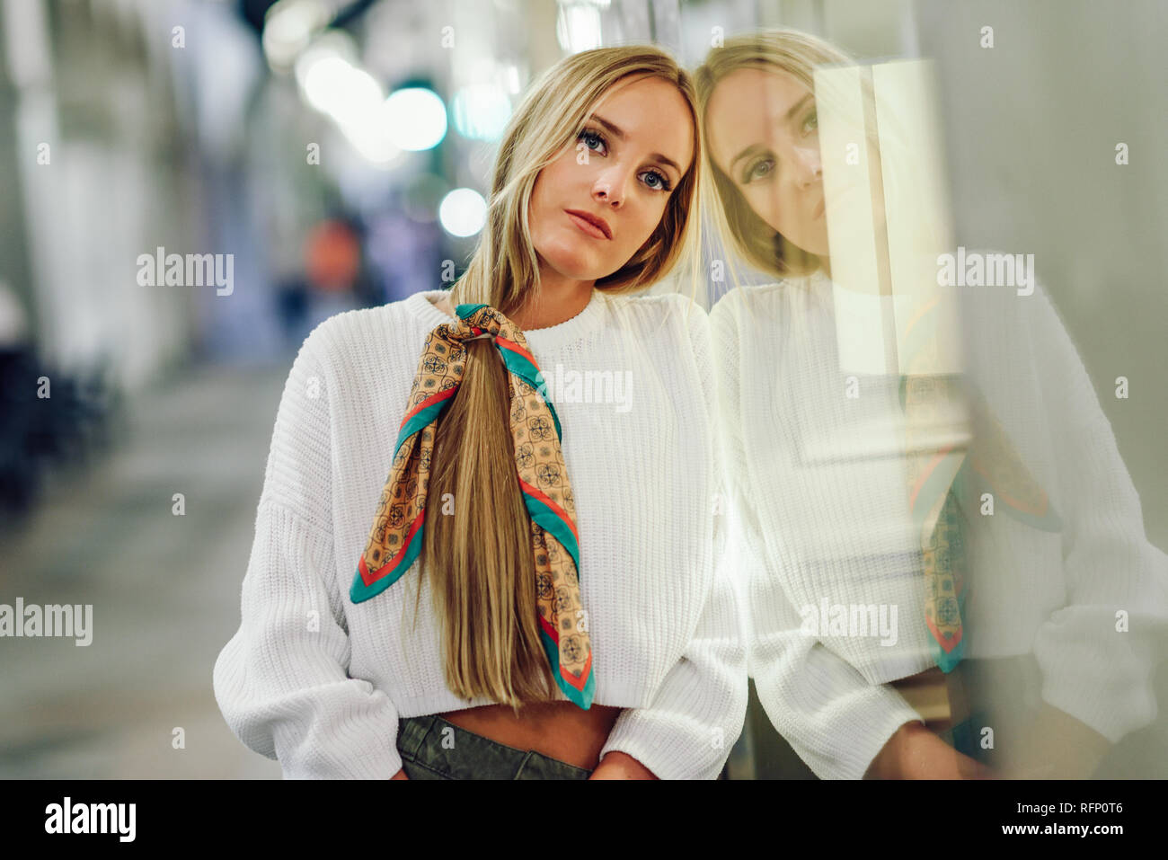 Blonde Mädchen tragen weiße Pullover auf der Straße mit Defokussierten Lichter der Stadt im Hintergrund. Hübsche Frau mit Zopf Frisur bei Nacht re Stockfoto