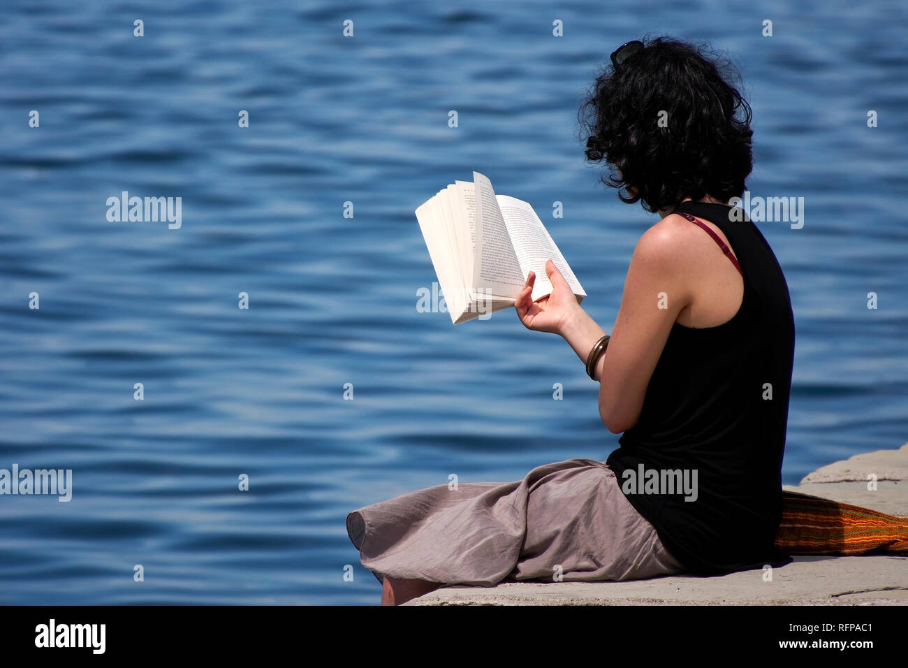 Ein Mädchen mit einem Buch am Rande des Pier sitzt Stockfoto