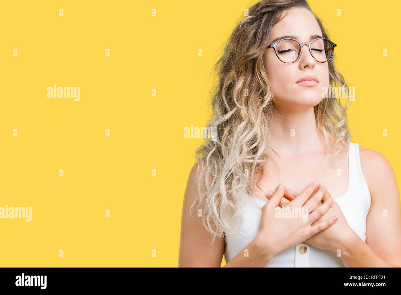 Schöne junge blonde Frau Brille über isolierte Hintergrund lächelnd mit der  Hand auf der Brust mit geschlossenen Augen und dankbare Geste auf das  Gesicht. Gesundheit Stockfotografie - Alamy
