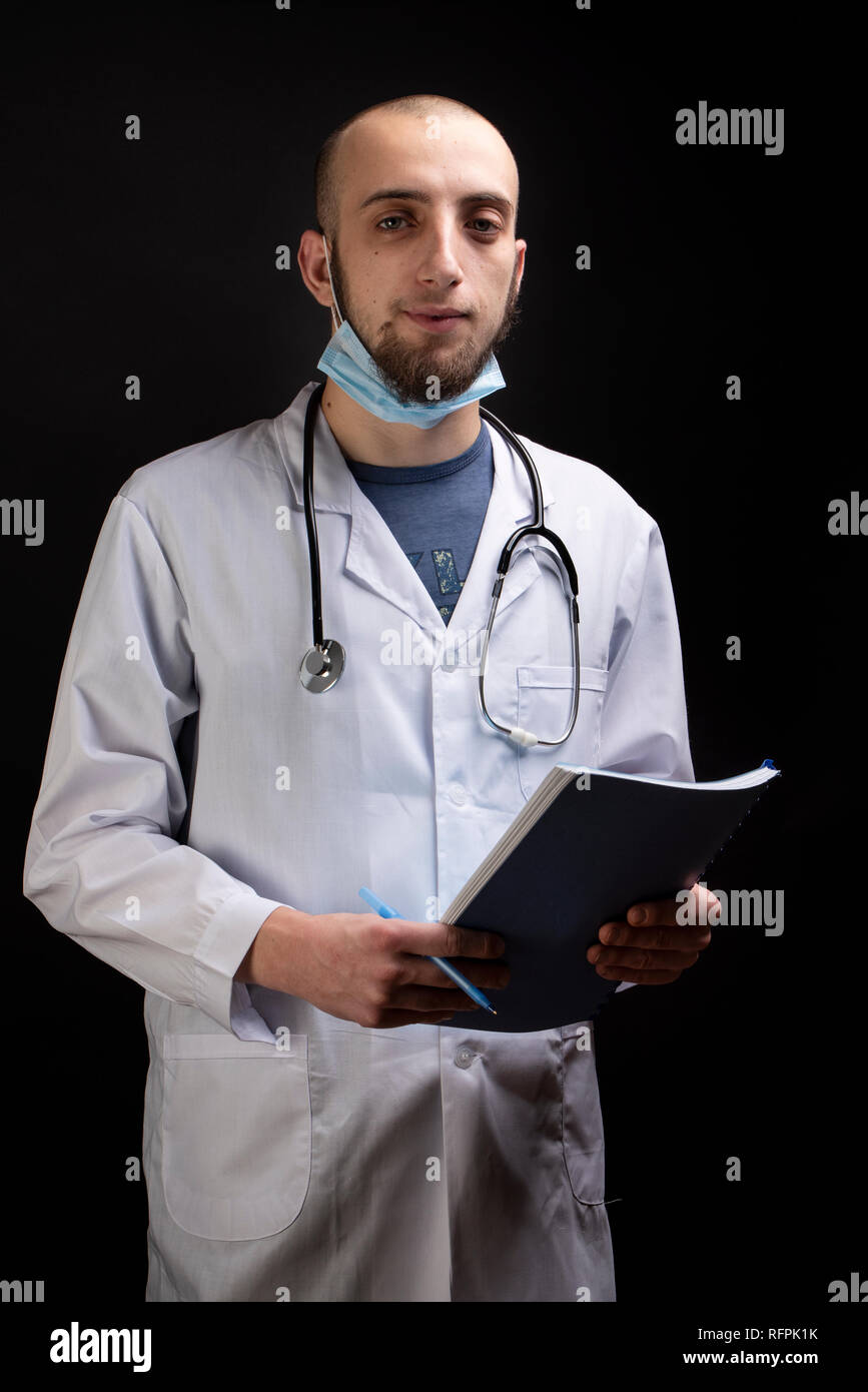 Junge männliche Arzt mit Stethoskop, Maske, die eine Datei und Blick in die Kamera. Arzt Beruf Stockfoto