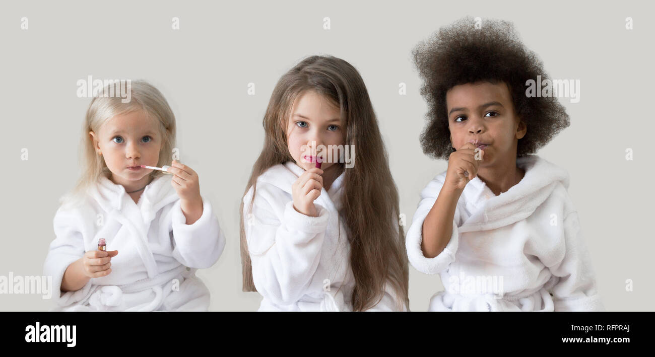 Drei Mädchen Freundinnen Lippenstift. Kinder verschiedener Nationalitäten in weißen Kitteln spielen mit dem Kometen der Eltern. Stockfoto