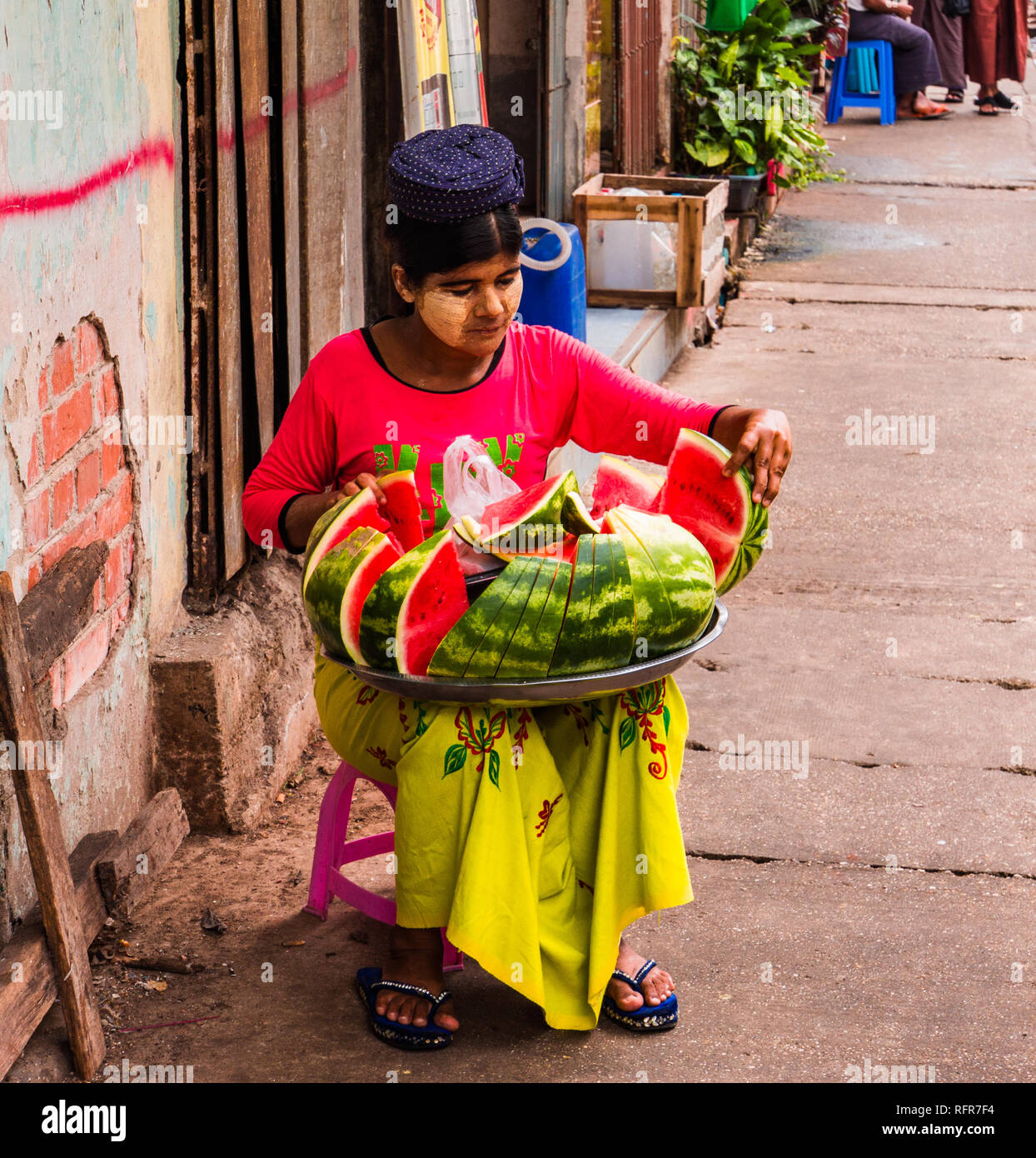 Burmesischen Frau mit Thanaka kosmetische Einfügen auf ihrem Gesicht sitzt auf dem Bürgersteig verkaufen Scheiben Wassermelone Stockfoto