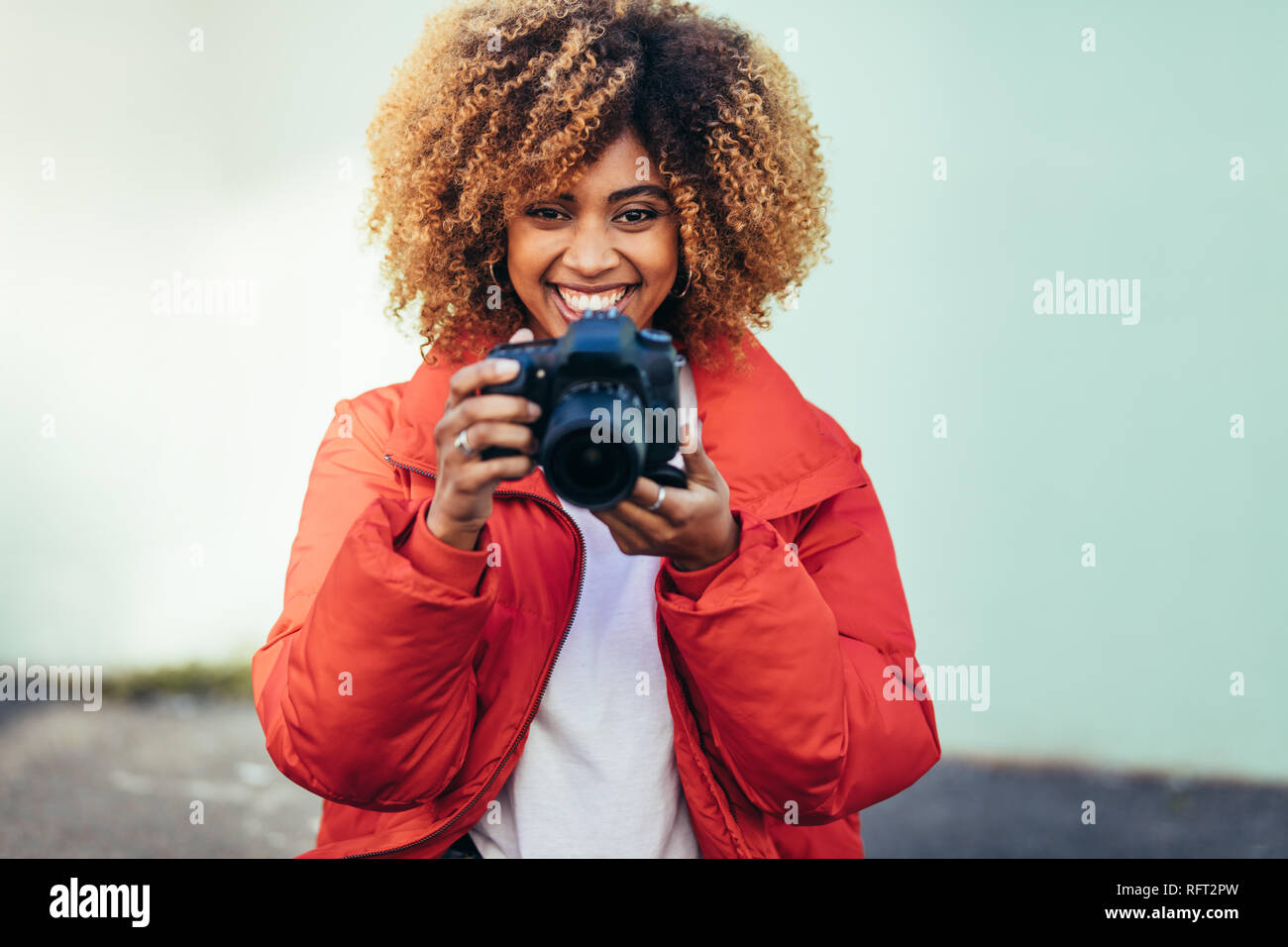 Porträt einer fröhlichen afro-amerikanische Frau mit einer DSLR-Kamera. Weibliche Reisende Fotografieren im Freien mit einer digitalen Kamera. Stockfoto