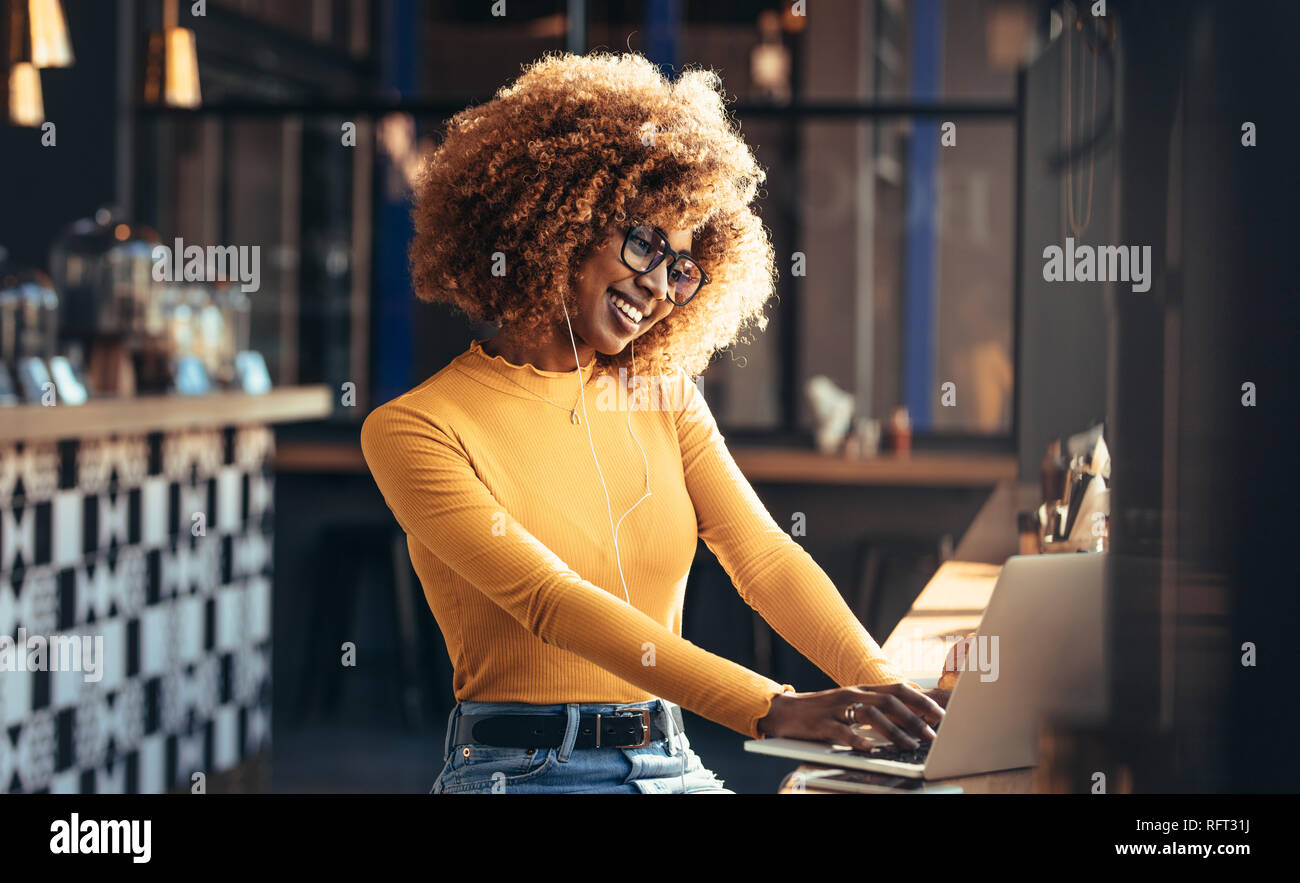 Weibliche Unternehmer arbeiten am Laptop sitzen in einem Restaurant und Musik zu hören. Lächelnd afro-amerikanische Frau an einem Cafe mit Ihrem Laptop. Stockfoto