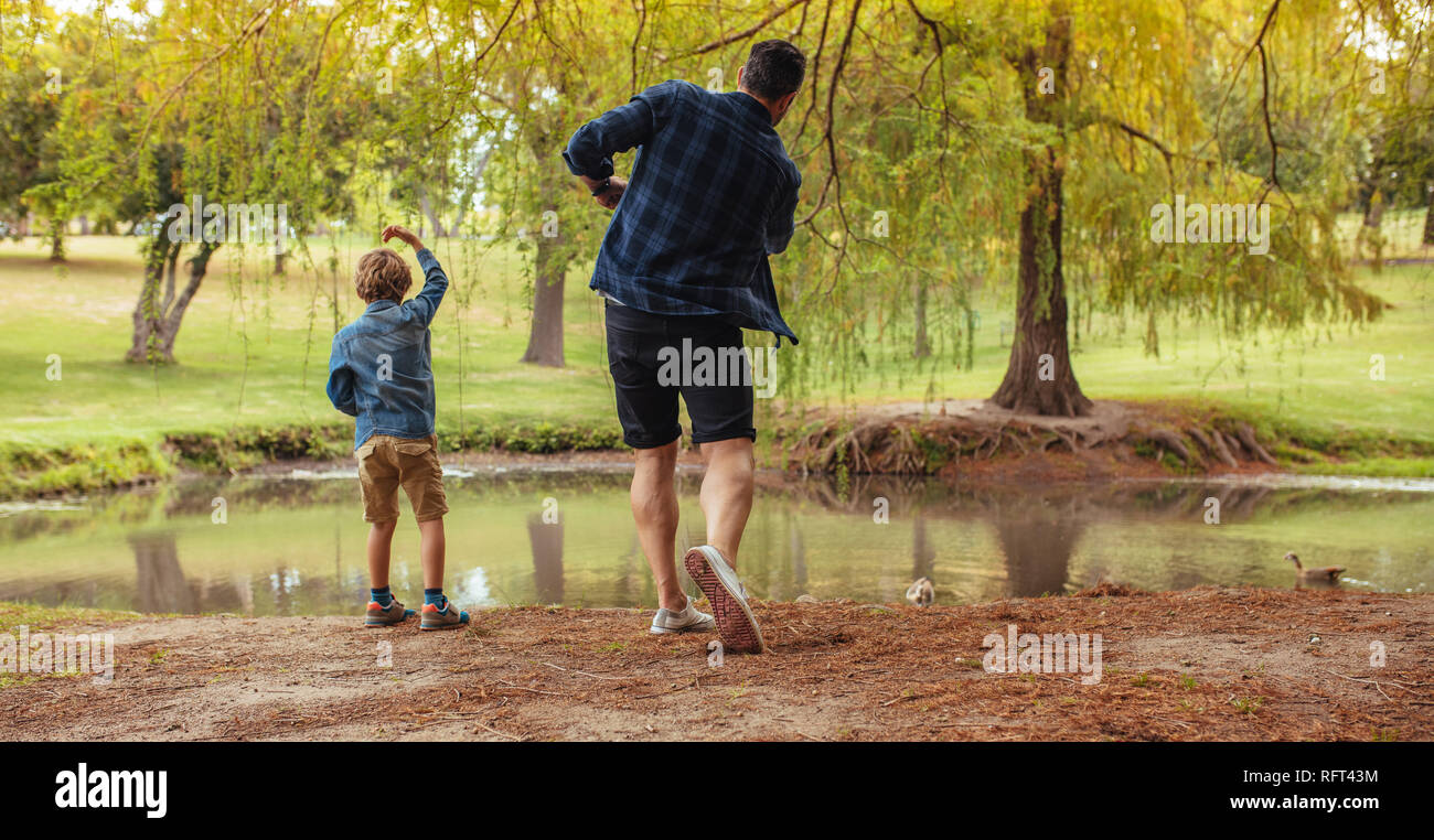 Ansicht der Rückseite des Vater und Sohn werfen Steine in den Teich im Park. Mann und kleinen Jungen Spaß im Park. Kind mit Vater werfen Steine in den Teich. Stockfoto