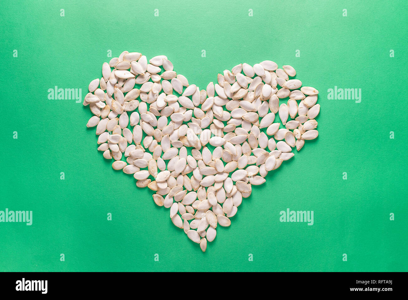 Herz Form der Kürbiskerne auf grünem Hintergrund. Minimalistischer flach Komposition. Stockfoto