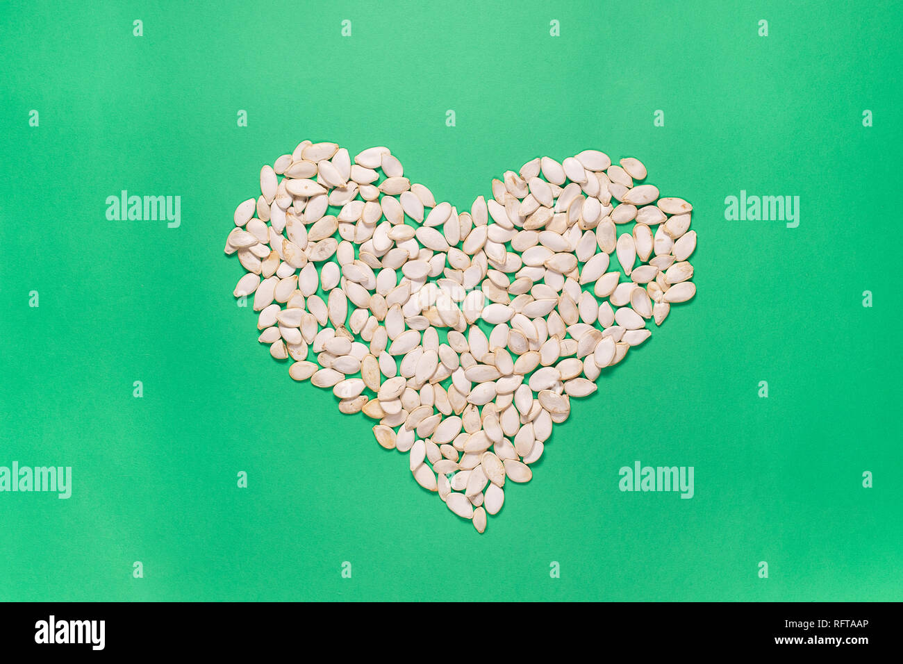 Herz Form der Kürbiskerne auf grünem Hintergrund. Minimalistischer flach Komposition. Hartes Licht. Stockfoto