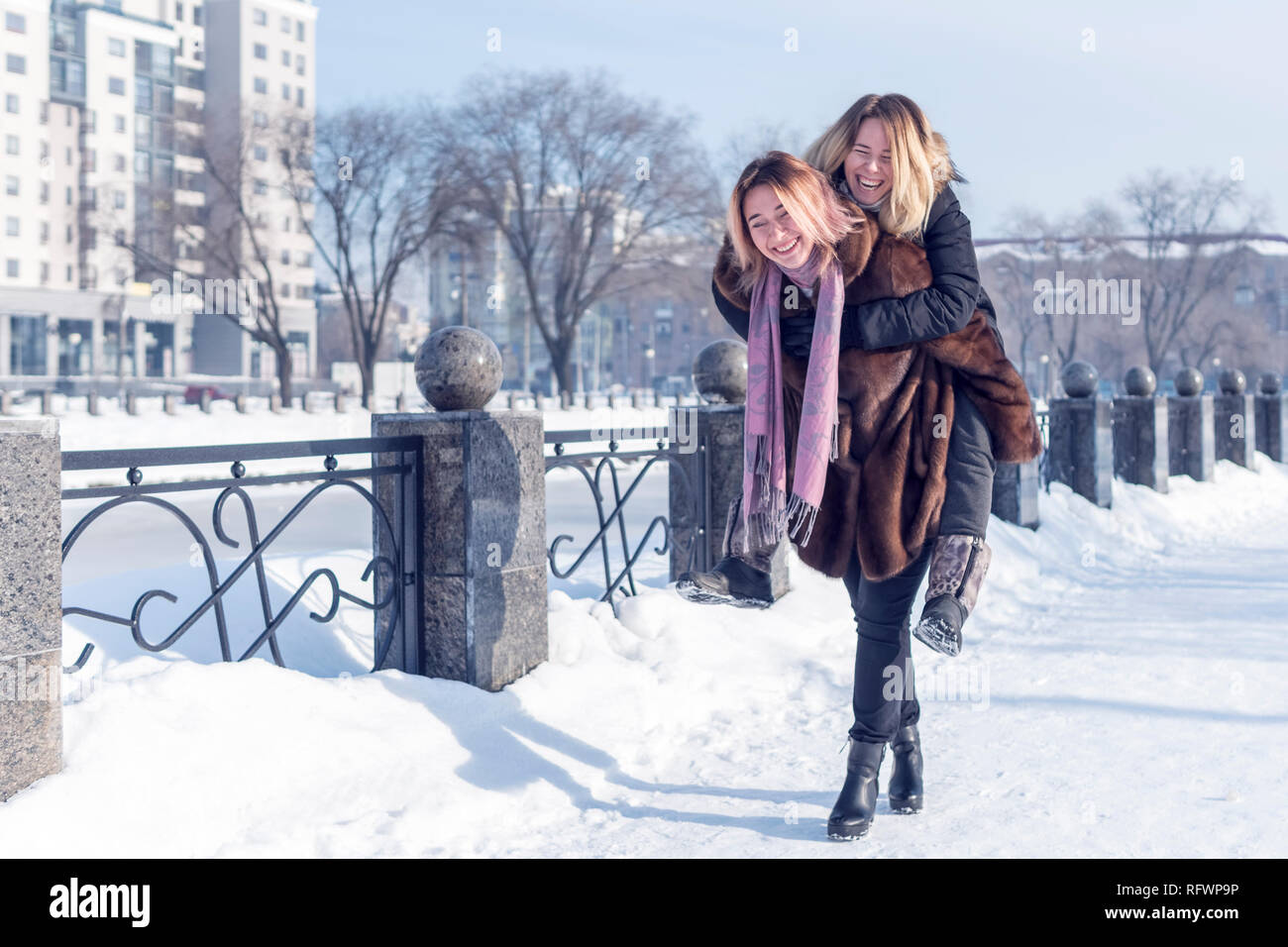 Eine Frau sprang auf den Schultern eines anderen beim laufen entlang einer winter Kai von einem zugefrorenen Fluss Stockfoto