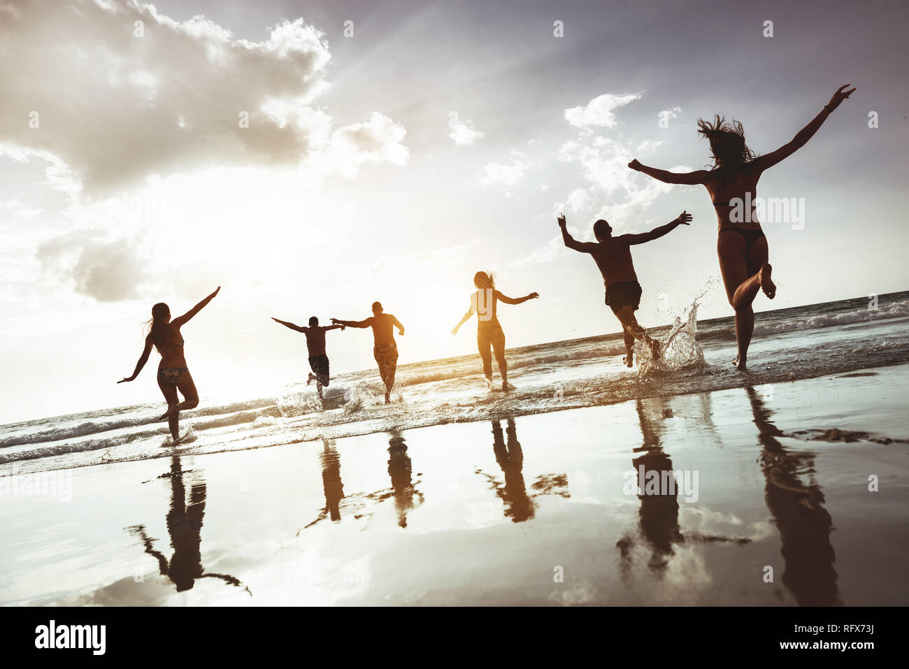 Große Gruppe der glückliche Freunde läuft und springt im Sunset Beach. Sechs aktive Silhouetten gegen Meer Strand Stockfoto