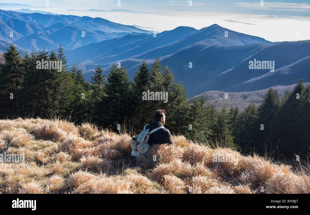 Ein Mann Wanderer tragen vintage Rucksack allein sitzend bewundern die Berglandschaft im Winter. Stockfoto
