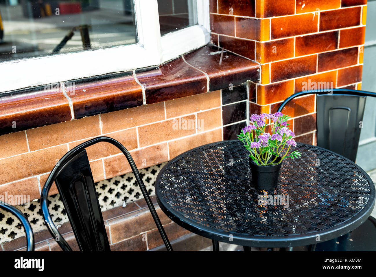 Nahaufnahme des leeren Tisch draußen Restaurant Backsteingebäude cafe Metall Stuhl auf Bürgersteig Straße mit lila Blüten Blumentopf versenkt Einstellung und niemand Stockfoto
