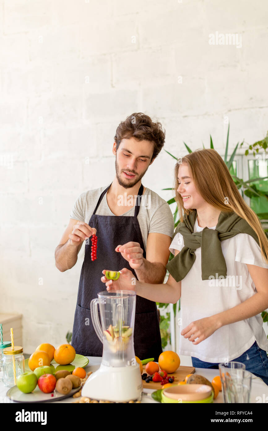 Positive fröhlicher junger Mode Leute hinzu Beeren und Kiwi zu einem Entsafter Stockfoto