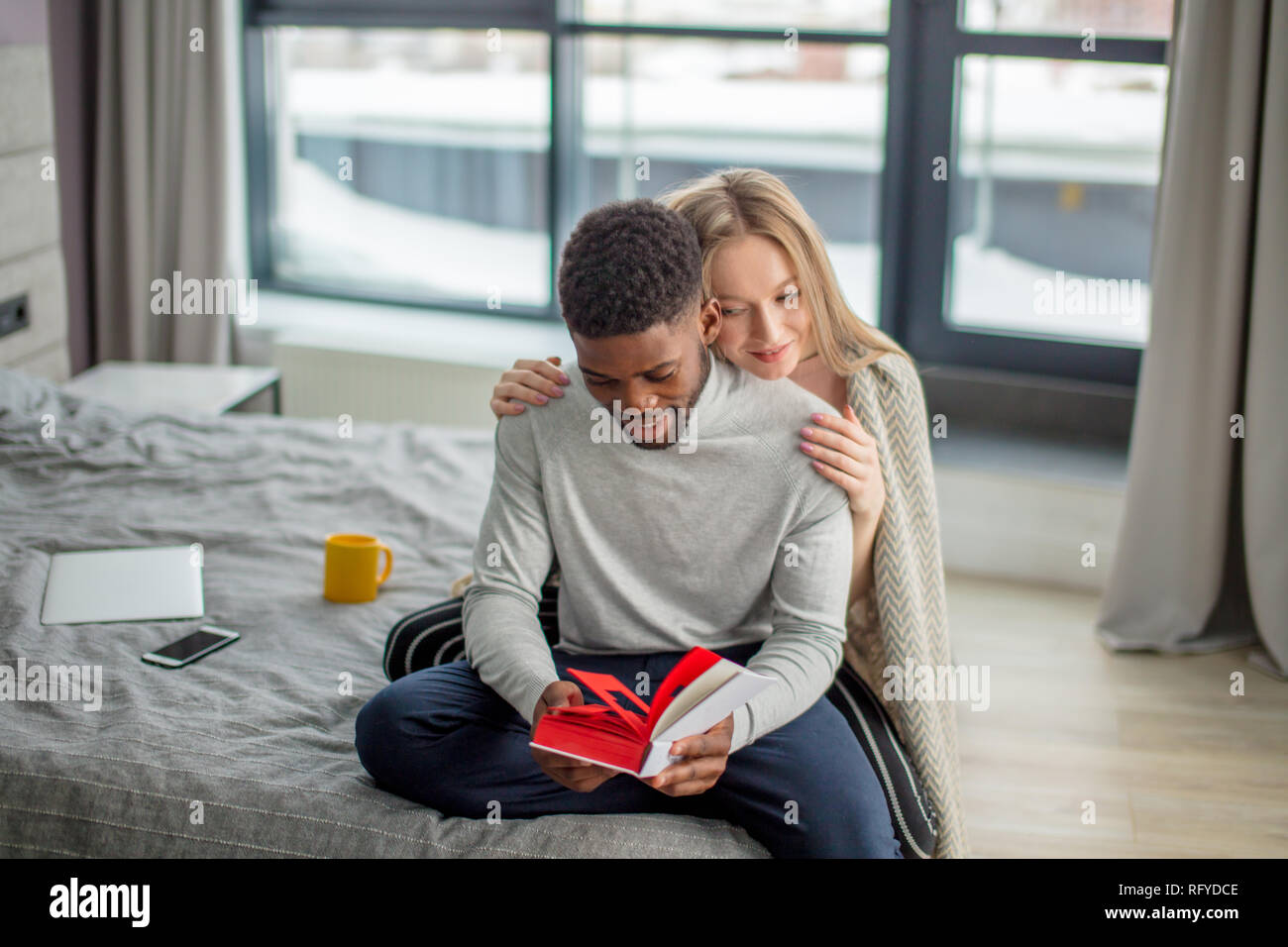 Happy interracial Paare verbringen Wochenende zusammen zu Hause, entspannen mit Buch Stockfoto
