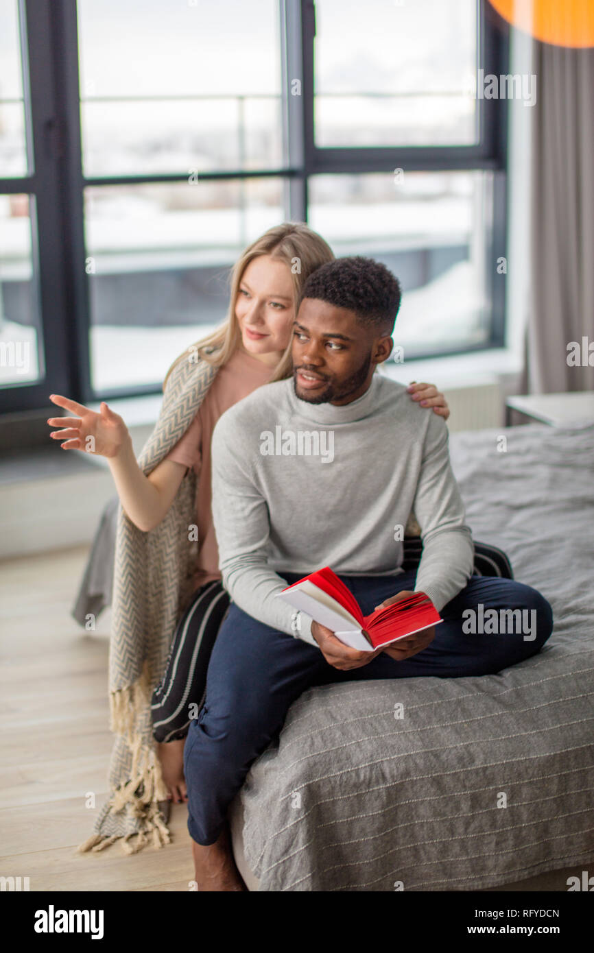 Happy interracial Paare verbringen Wochenende zusammen zu Hause, entspannen mit Buch Stockfoto