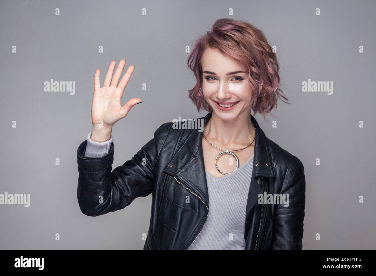 Portrait von aufgeregt, schöne Mädchen mit kurzen Frisur und Make-up in schwarzem Leder Jacke stehend, Begrüßung und Kamera mit toothy Lächeln. Stockfoto