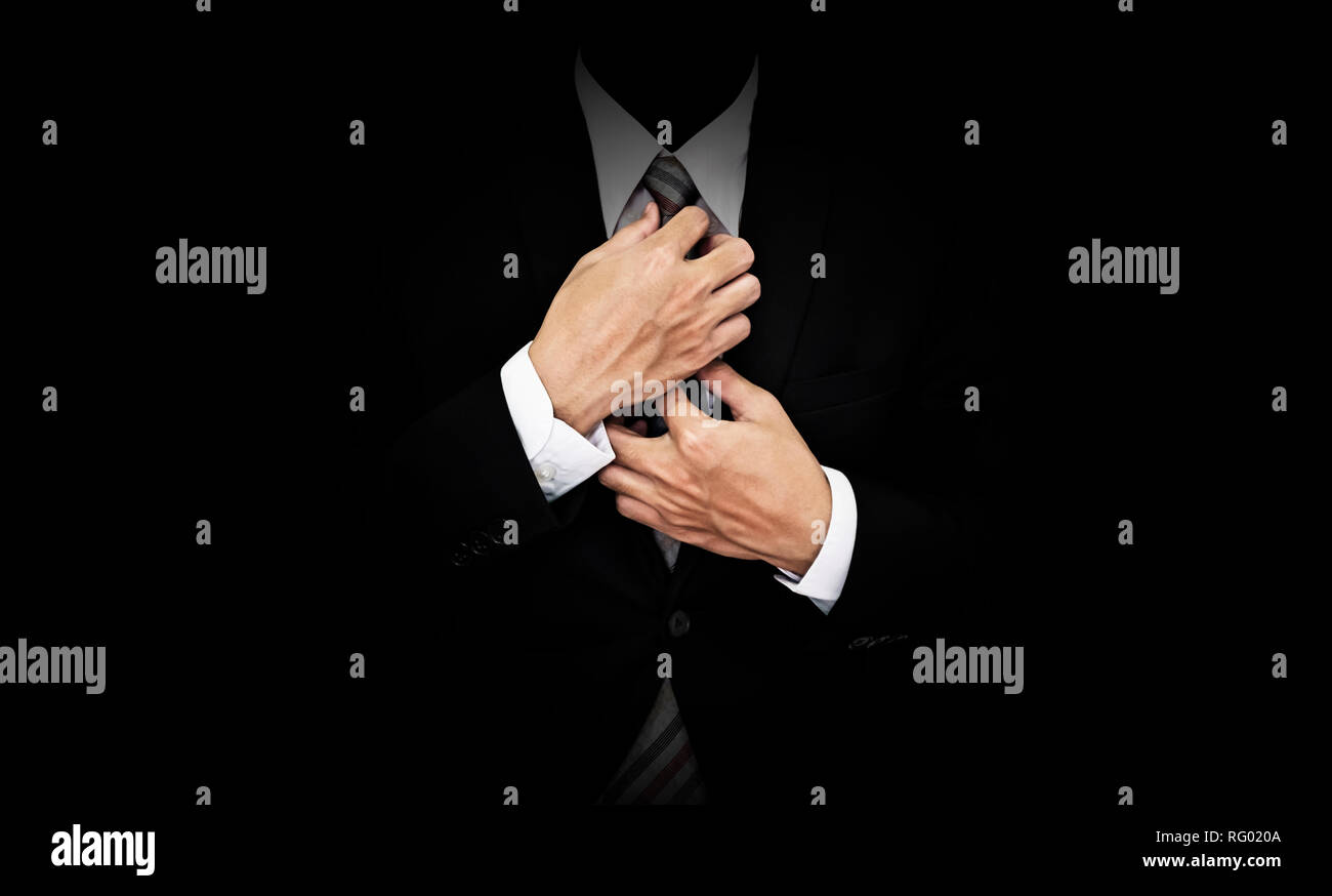 Unternehmer im schwarzen Anzug Krawatte binden, auf schwarzem Hintergrund Stockfoto