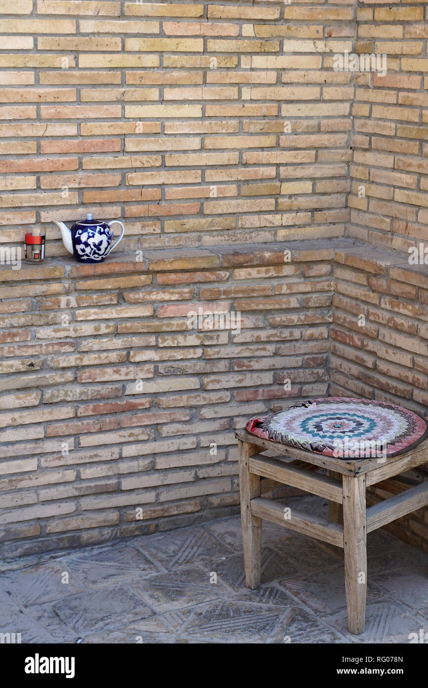 Teekannen mit Glas an der Ziegelwand und antiken Holzhockern mit Sitzmatte, Taschkent, Usbekistan Stockfoto