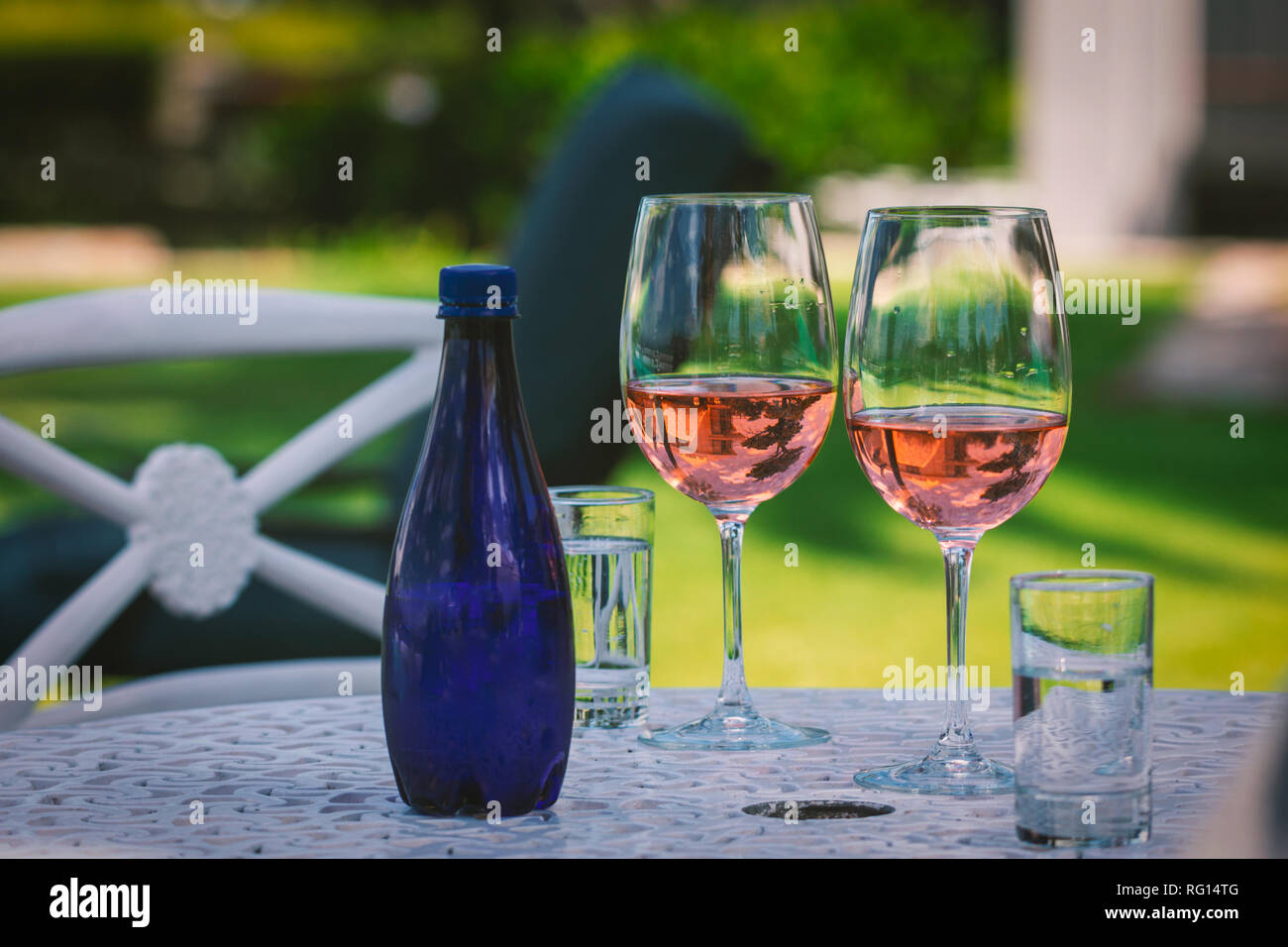 Zwei Gläser mit Rose Wein und blaue Flasche Wasser auf dem Tisch im Garten Stockfoto