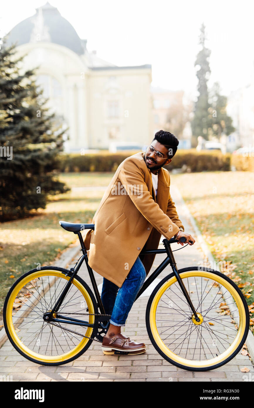 Seitenansicht eines indischen hipster Mann im Mantel zu Fuß mit dem Fahrrad auf einer Straße der Stadt Stockfoto
