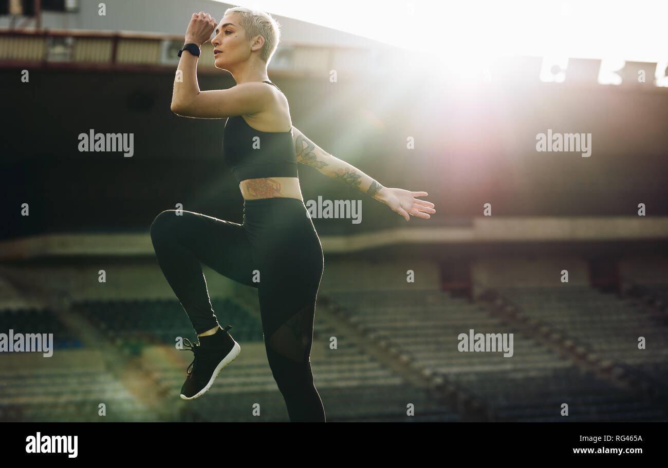 Frau tun high Knee Lifts in einem Stadion mit Sonne in den Hintergrund. Frau in Fitness Kleidung Arbeiten in einem Leichtathletik Stadion. Stockfoto